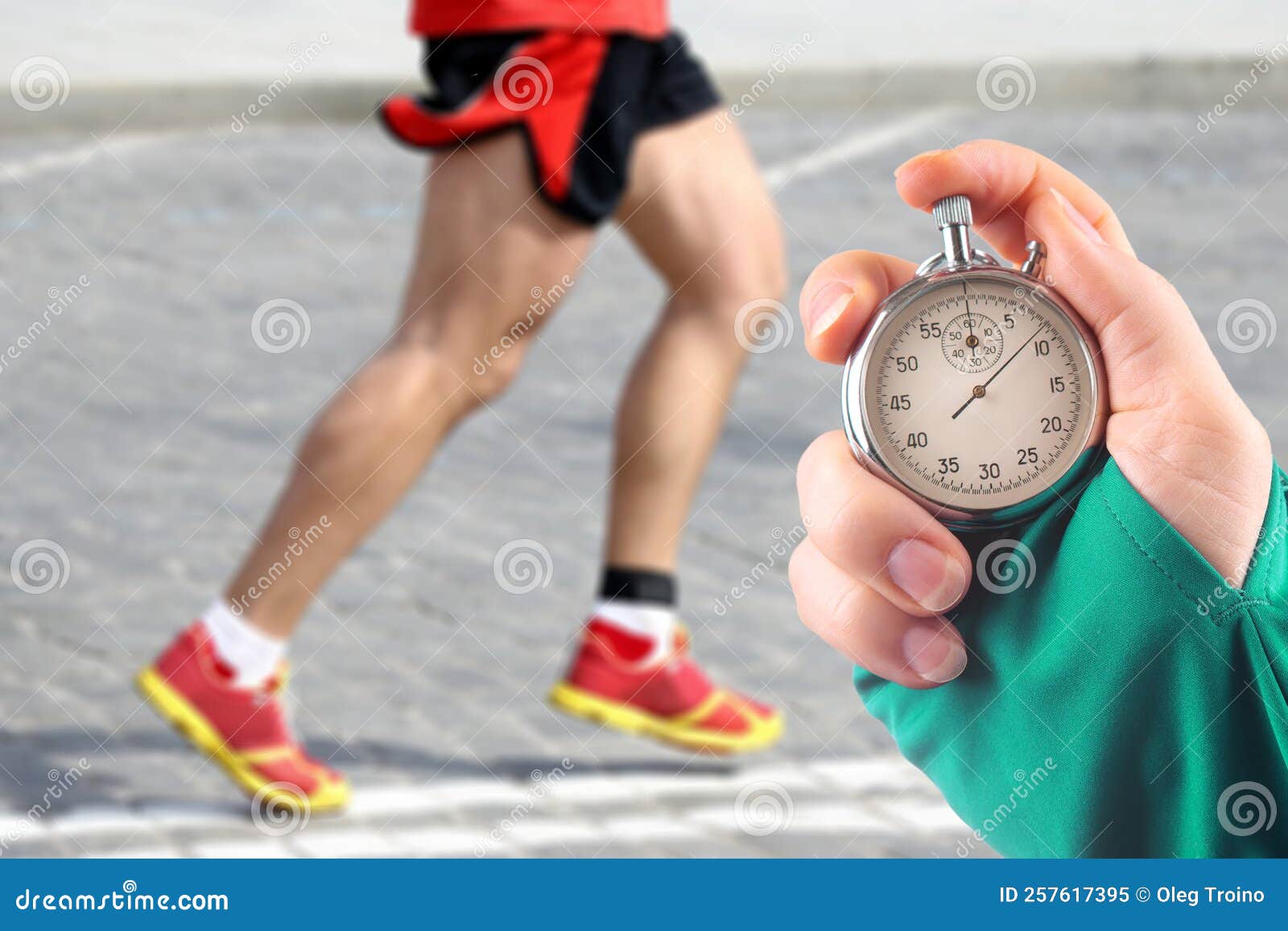 Measuring The Running Speed Of An Athlete Using A Mechanical Stopwatch. Hand With A Stopwatch On The Background Of The Legs Of A Runner. Stock Photo, Picture and Royalty Free Image. Image