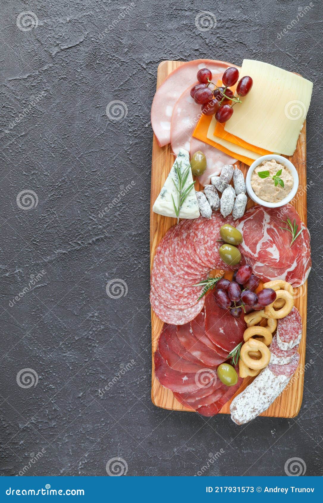 meat board with products from the italian region to wine - sausages, cheeses, bread, fresh vegetables, green herbs, and grapes -