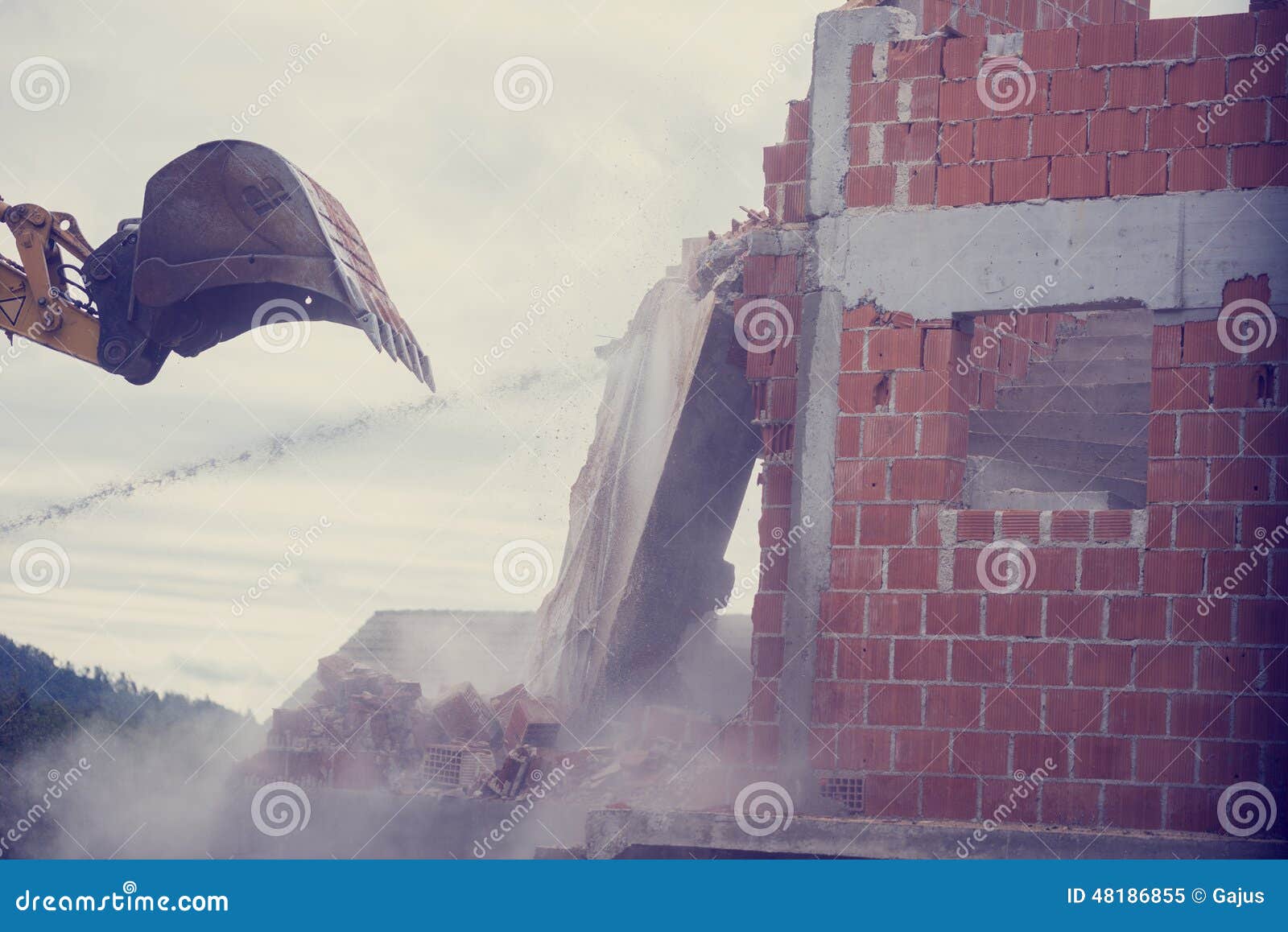 mechanical digger demolishing the wall of a brick building