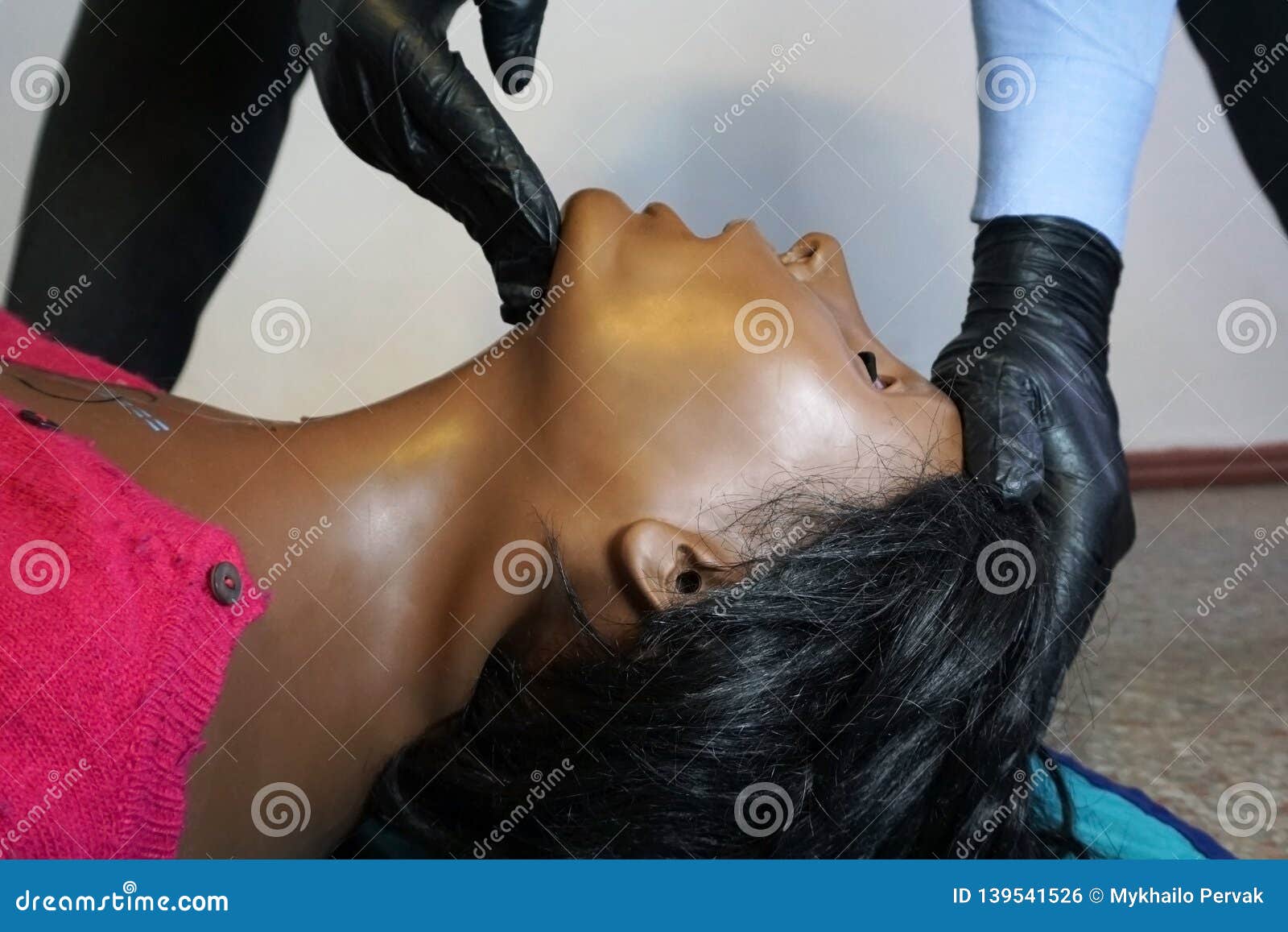medical stuff in a black gloves performing `clear and open tha airway` head tilt - chin lift on a simulation mannequin dummy