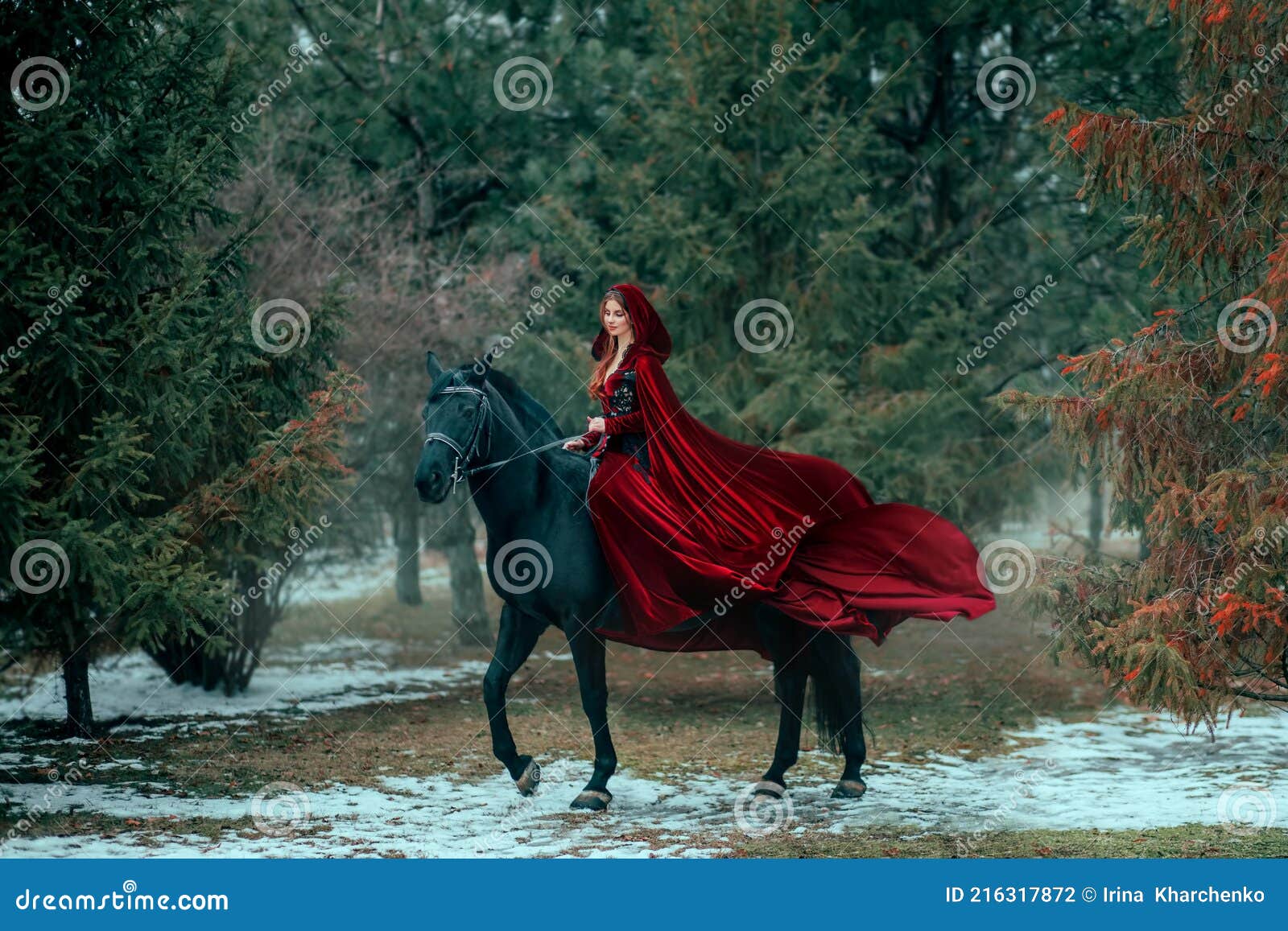medieval woman princess in red dress sits astride black steed horse. girl rider in vintage cloak cape train flies in
