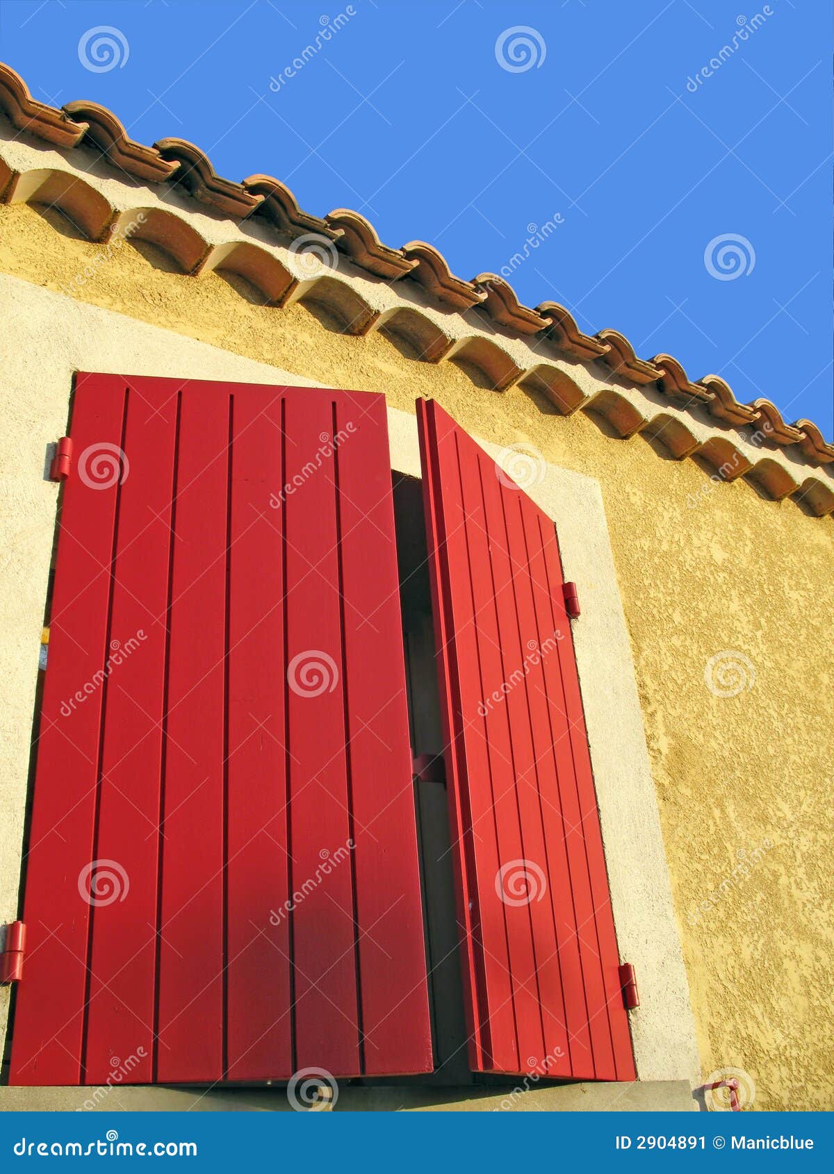 Mediterrane kleur. Abstract architecturaal schot van een hoekige buitenmuur met heldere rode blinden tegen een blauwe hemel.