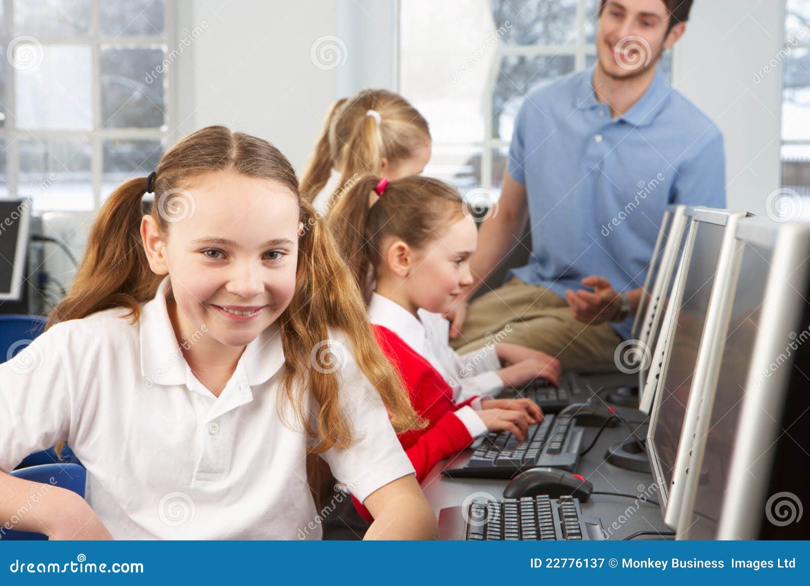 Meisje dat in schoolklasse aan camera glimlacht. Meisje dat in schoolklasse aan camera in computerzaal met leraar en andere studenten glimlacht