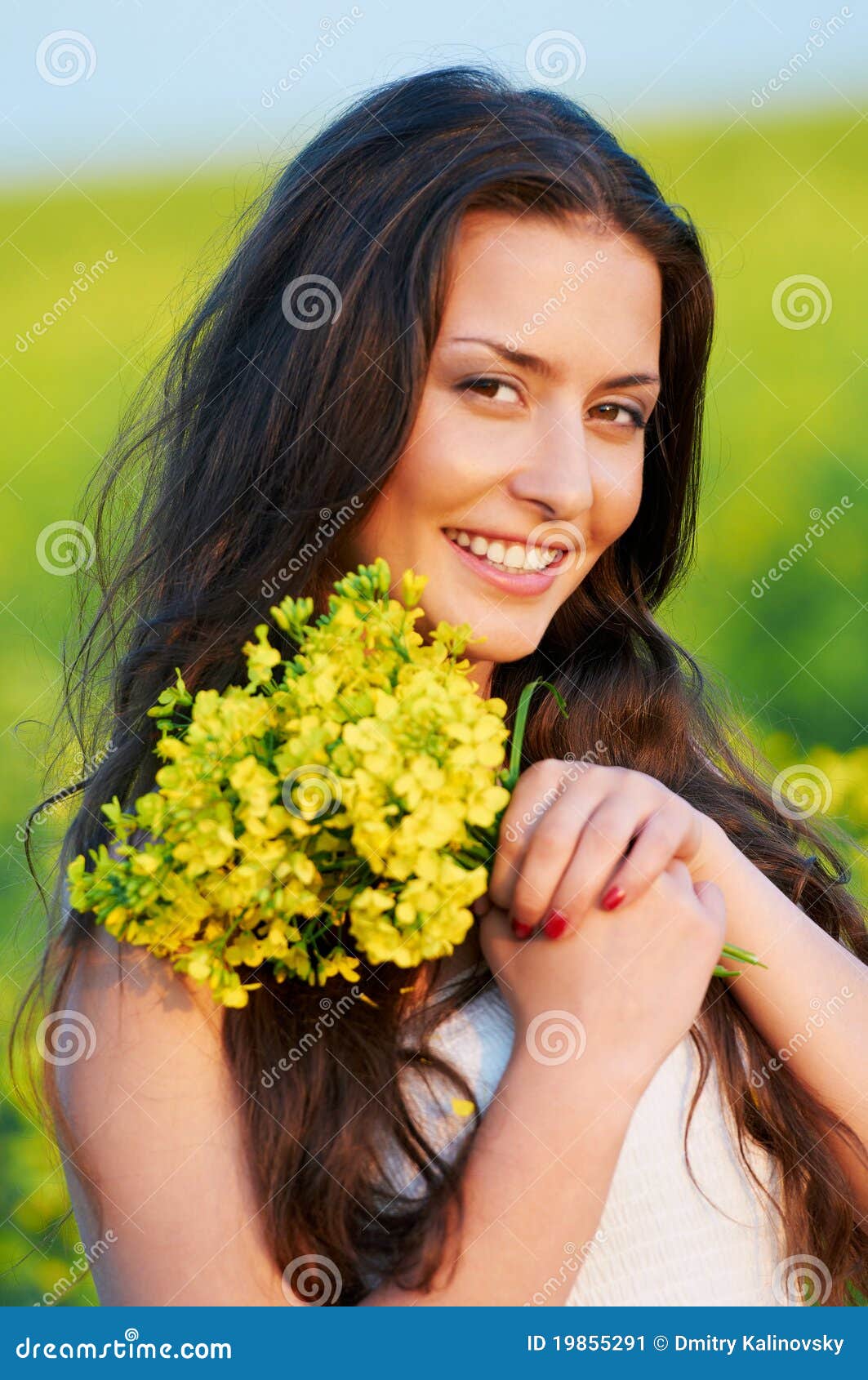 Meisje met bloemen bij de zomergebied. Gelukkige glimlachende jonge vrouw met bloemboeket over geelgroene verkrachtingsweide
