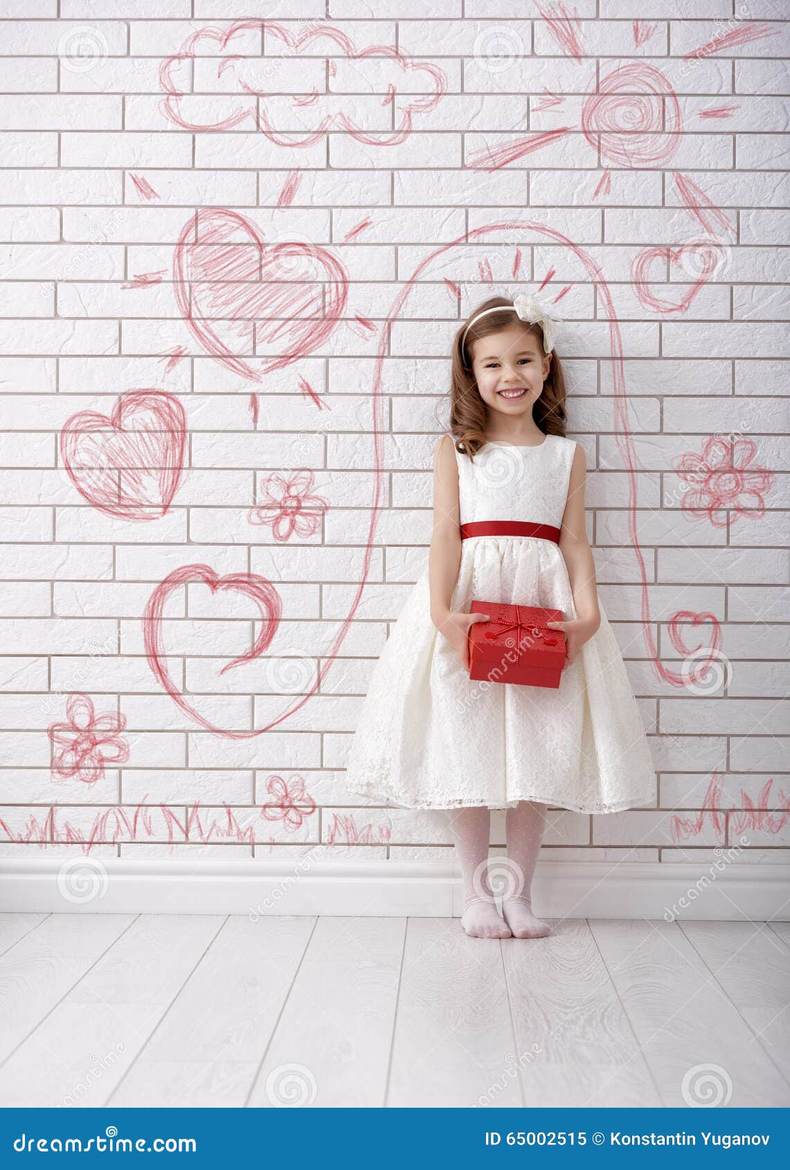 Zoet kindmeisje met rode giftdoos Het gelukkige meisje met de gift van Valentine bij bakstenen muur schilderde met de tekeningen van kinderen Huwelijk, Valentine-concept