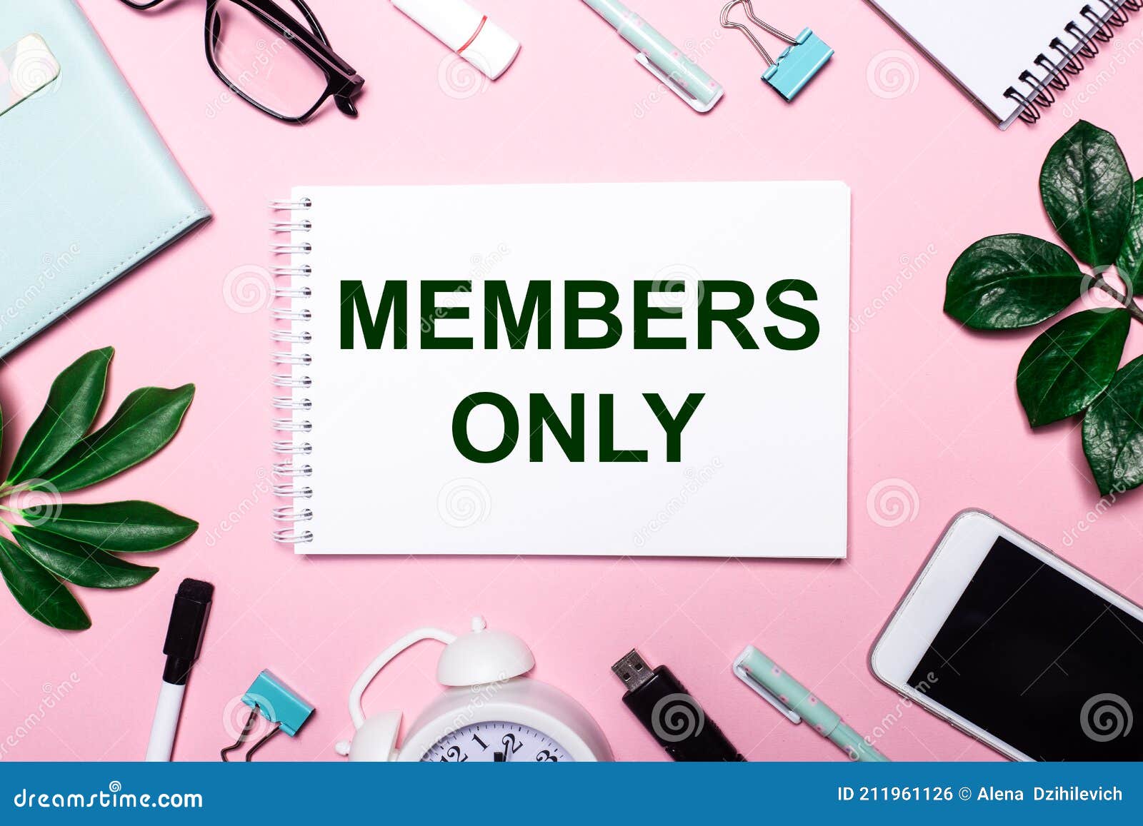members only is written in a white notebook on a pink background surrounded by business accessories and green leaves