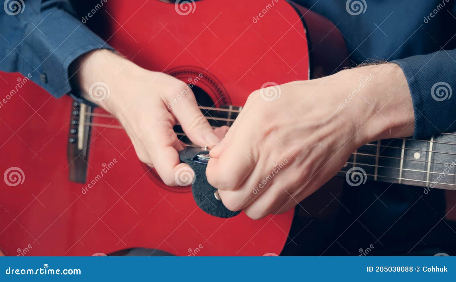 men hands in blue shirt hold a red guitar and take out pick