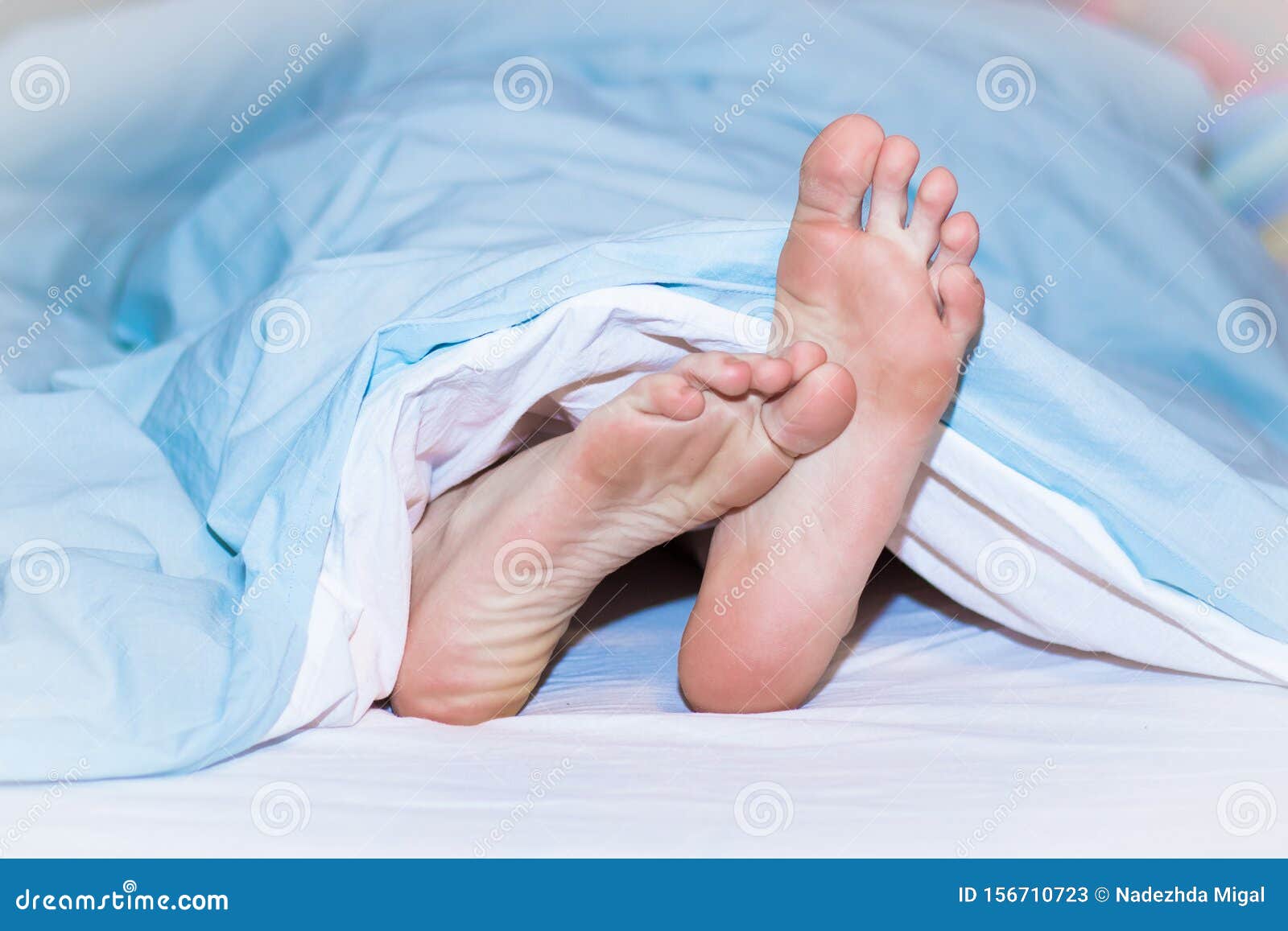 Men`s Feet Sticking Out from Under the Blue Blanket. Stock Image