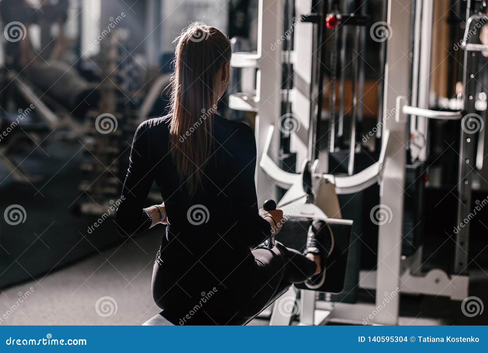 A menina atlética bonita vestida vestida em um sportswear preto está fazendo exercícios do esporte com equipamento no banco no gym moderno