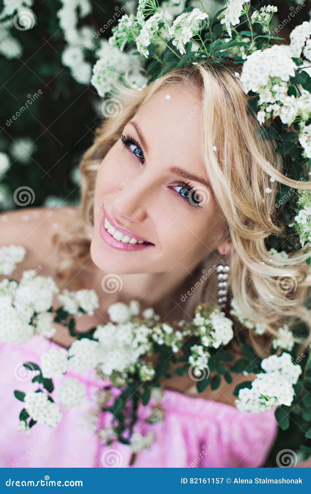 Menina com flores. Jovem mulher bonita com o jardim bonito ondulado longo do cabelo na primavera entre as flores brancas de florescência