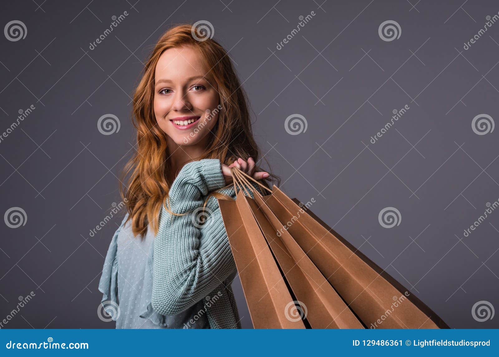 Menina do ruivo com sacos de compras. Menina de sorriso do ruivo na roupa azul com os sacos de compras, isolados no cinza