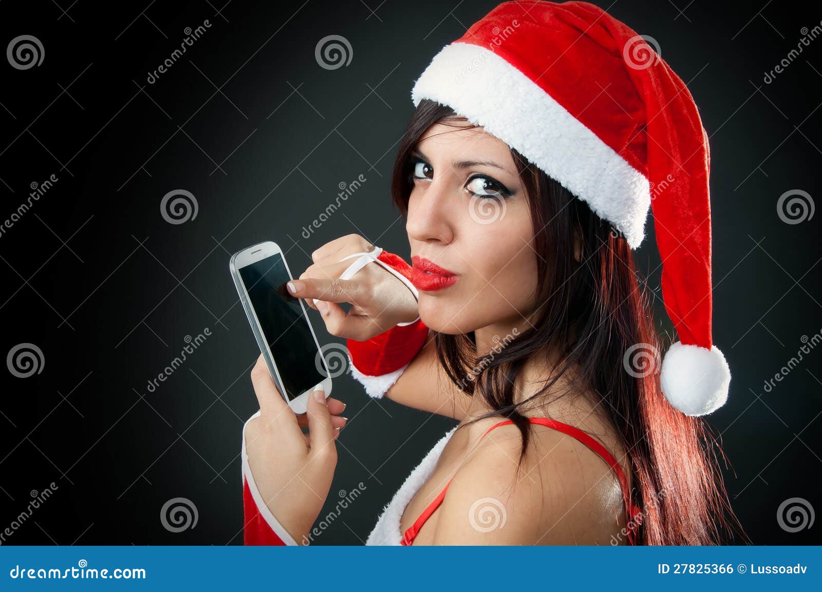 Menina que desgasta a roupa de Papai Noel com smartphone. O retrato da menina "sexy" bonita que desgasta Papai Noel veste-se com smartphone