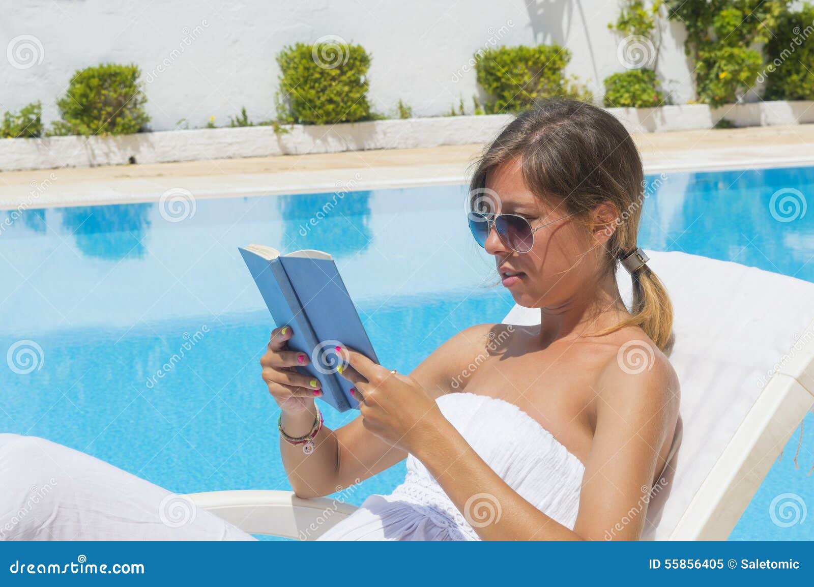 Menina que lê um livro ao tomar sol pela associação. Moça com leitura do chapéu de palha pela associação