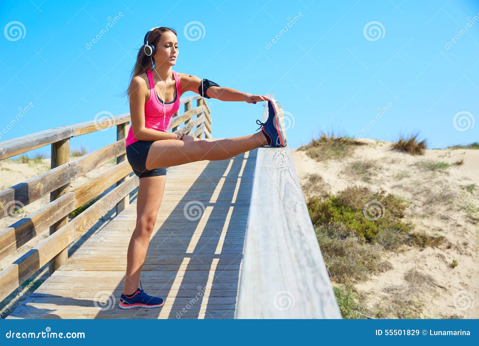 Menina running que estica em uma trilha da praia com headphores