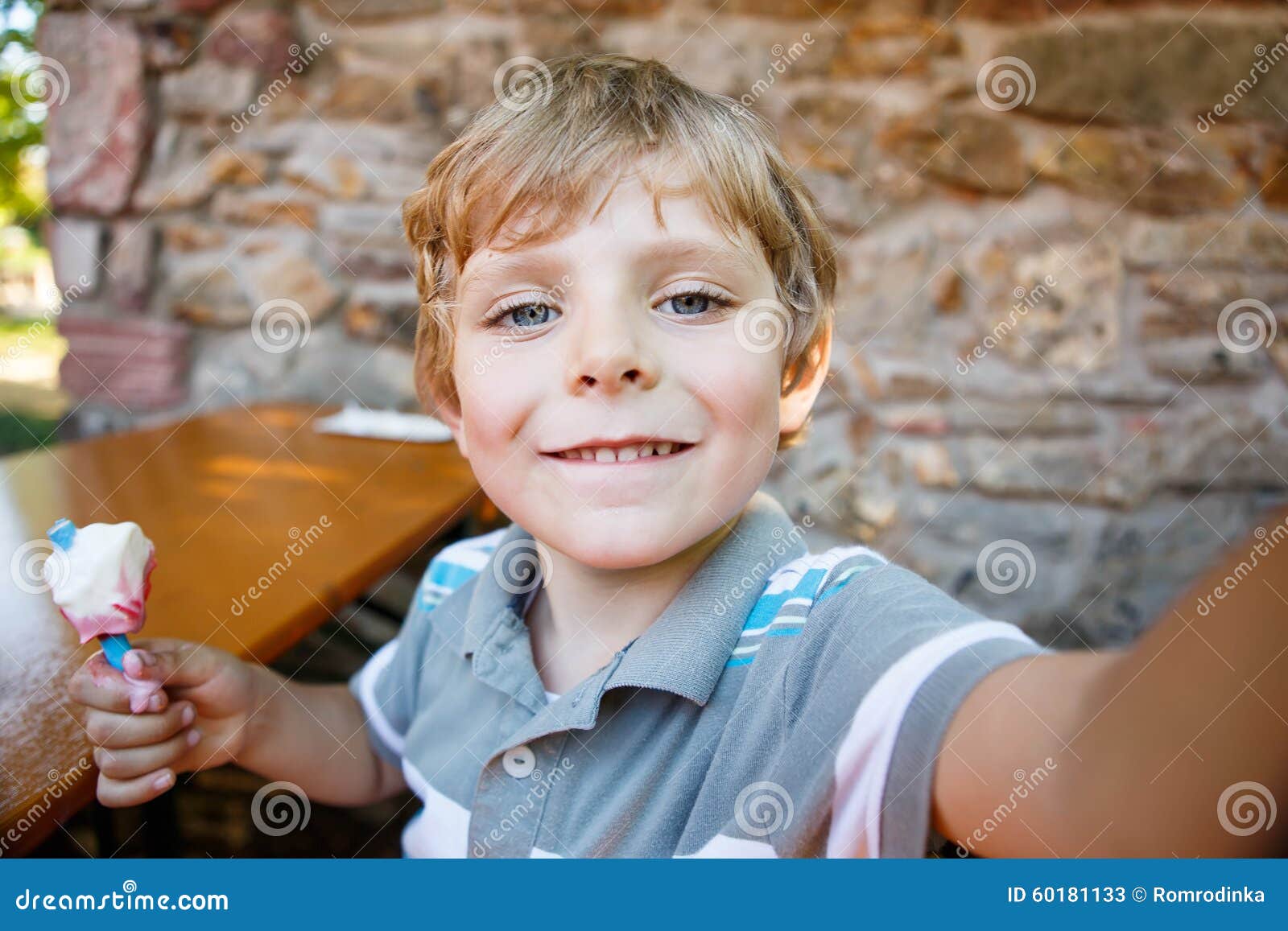 Menino da criança que toma o selfie com telefone celular. Caçoe o menino que toma o selfie com telefone celular durante comer o gelado no dia de verão criança loura feliz que tem o divertimento