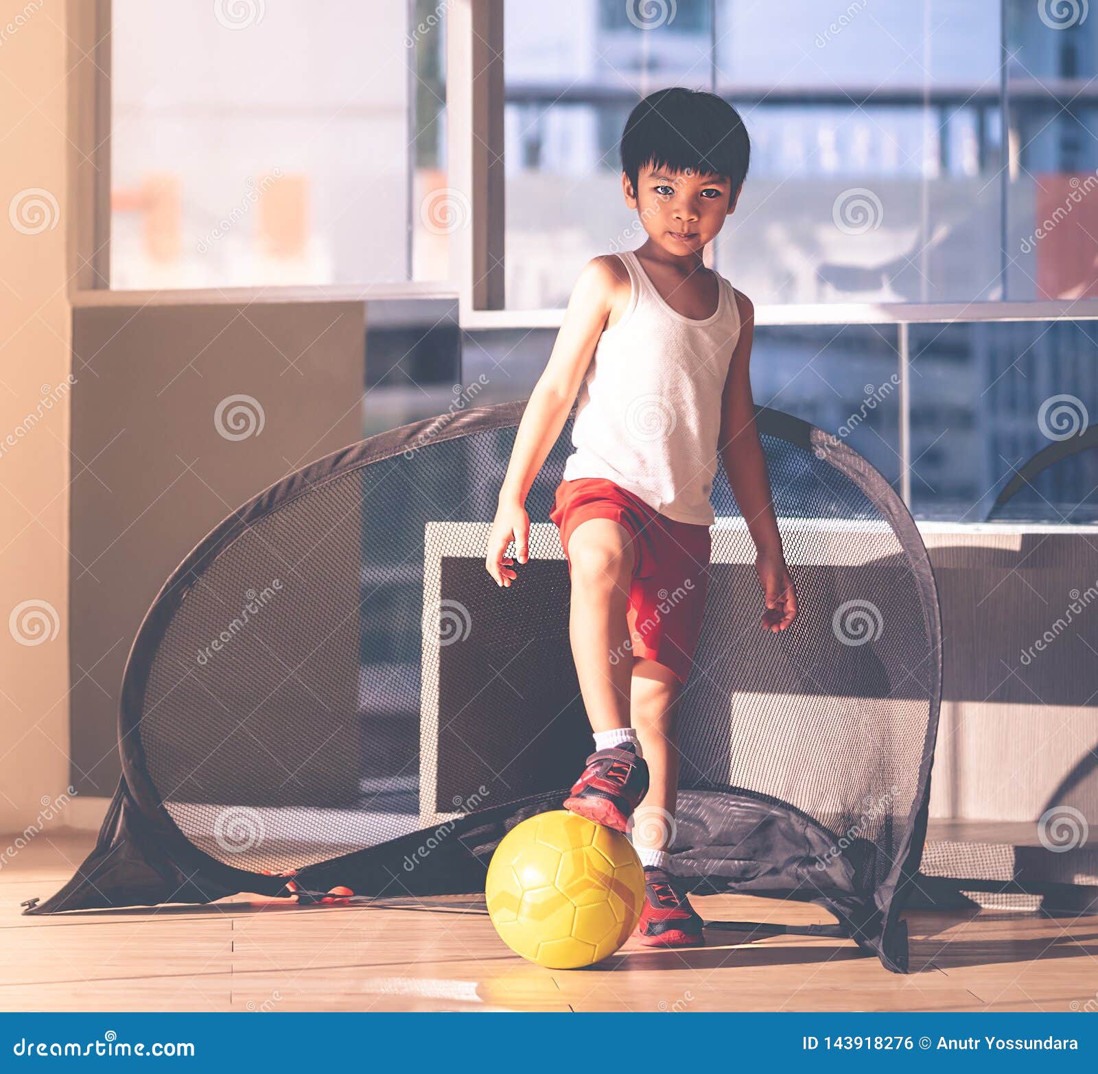 Menino Do Jogador De Futebol Que Pisa Na Bola Na Sala Imagem de