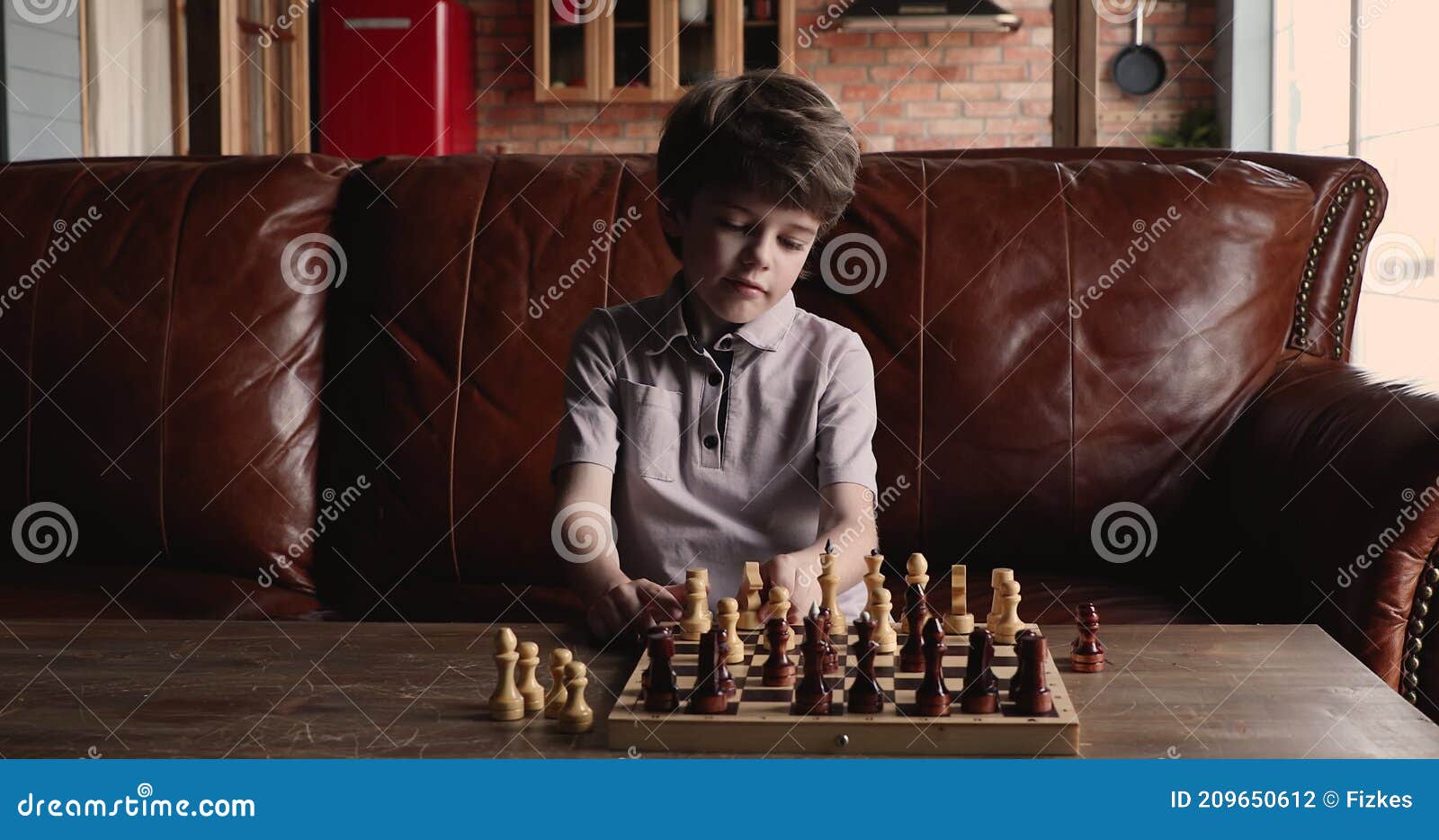 Menino ruivo de óculos sentado em casa e a jogar xadrez sozinho