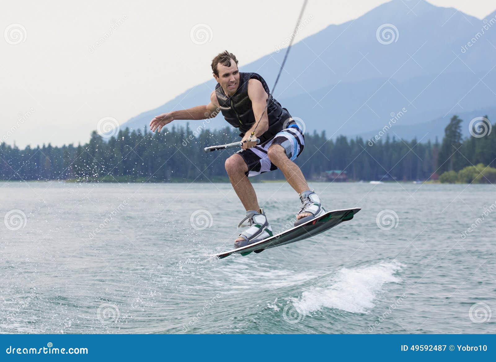 Mens het wakeboarding op een mooi bergmeer. Een actiefoto van een mens die over het kielzog op een wakeboard springen Het krijgen van wat grote lucht en het tonen van zijn vaardigheden