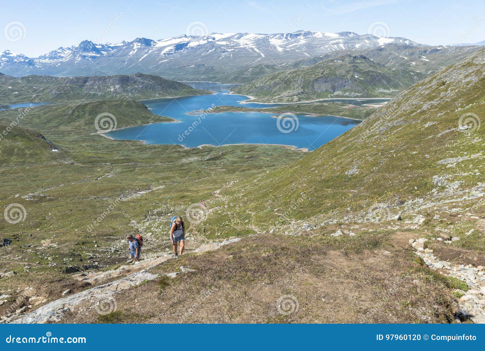 Mensen die in nationaal park in Noorwegen lopen. LEIRA, NOORWEGEN 19-07-2017: niet geïdentificeerde mensen die het het lopen spoor in nationaal park van bitihorn aan stavtjedtet met merenfjord en sneeuw op de bergen op 19-07-2017 lopen: de plaats waar er sneeuw in de zomer is