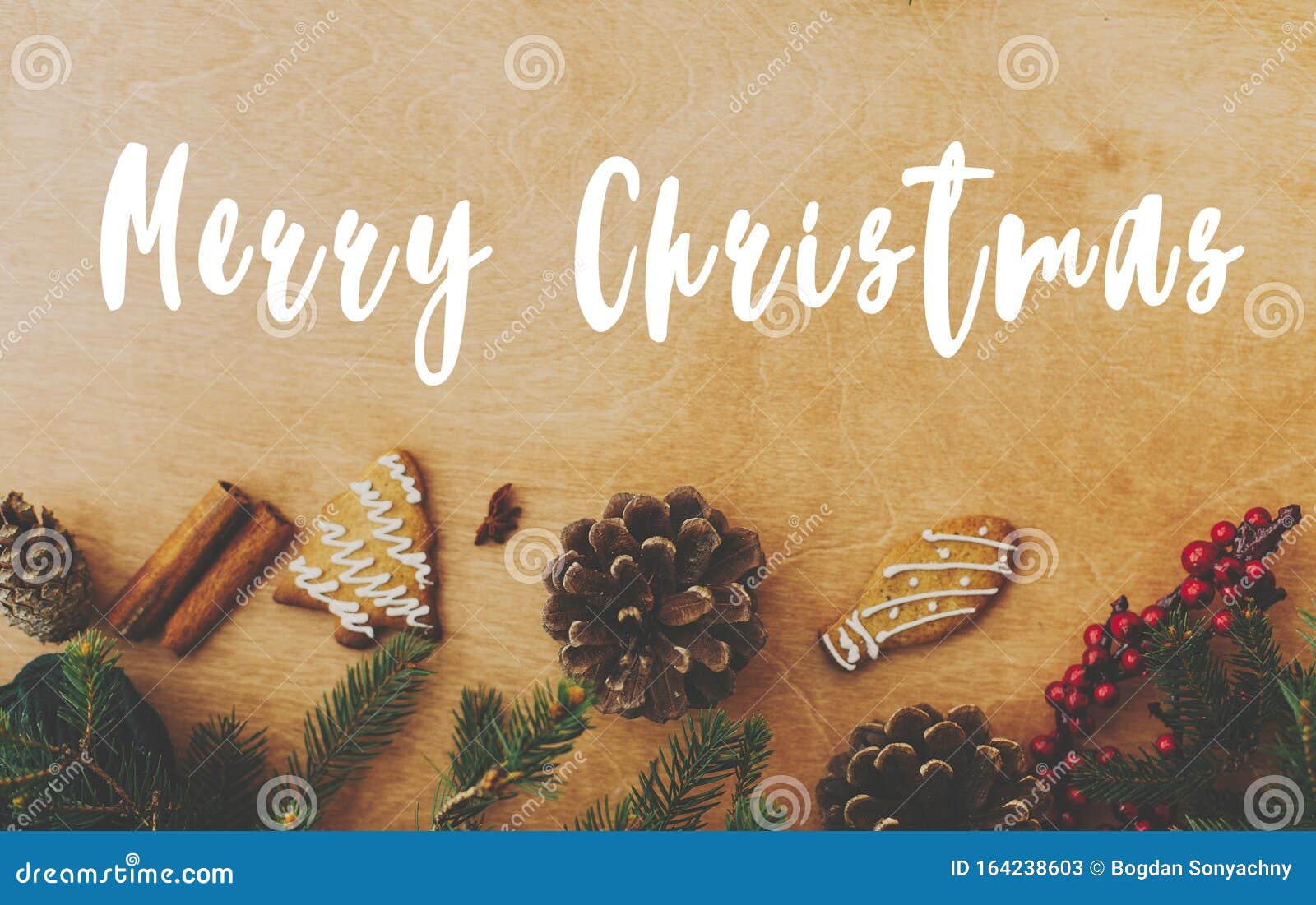 merry christmas text sign on stylish rustic frame of pine branches, cones, gingerbread cookies,thread, cinnamon, anise on rural