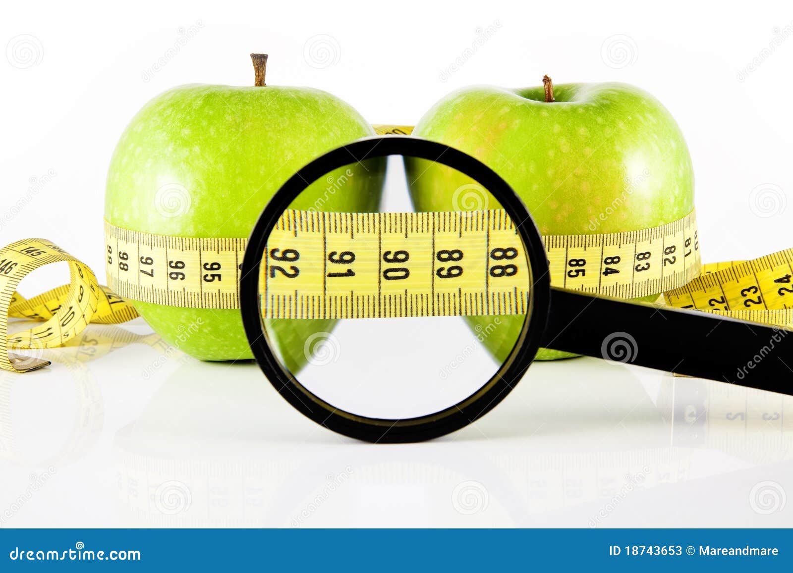 Messinstrument und Vergrößerungsglas mit zwei Äpfeln. Grüner Apfel zwei eingewickelt mit dem Messinstrument, auf einem weißen Hintergrund.