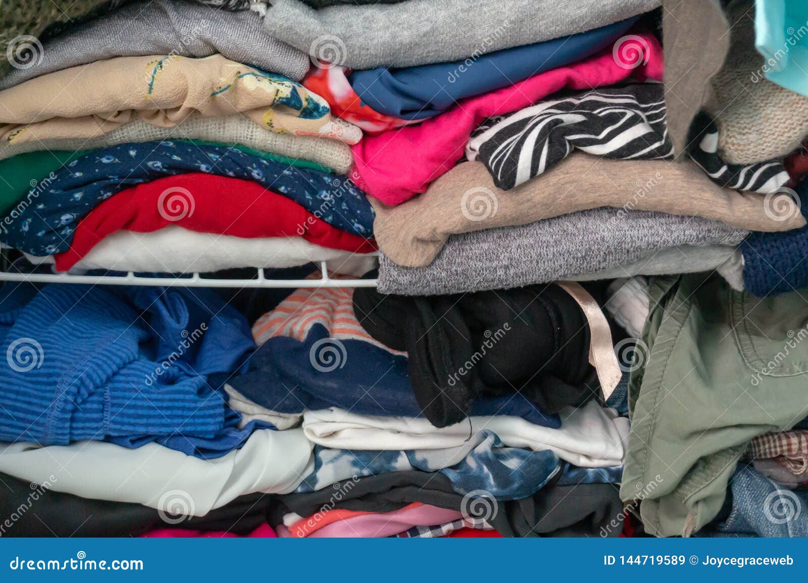 messy folded clothes crammed in a closet on a shelf. depicting woman`s wardrobe, consumerism, cleaning up, tidying up, purging, et