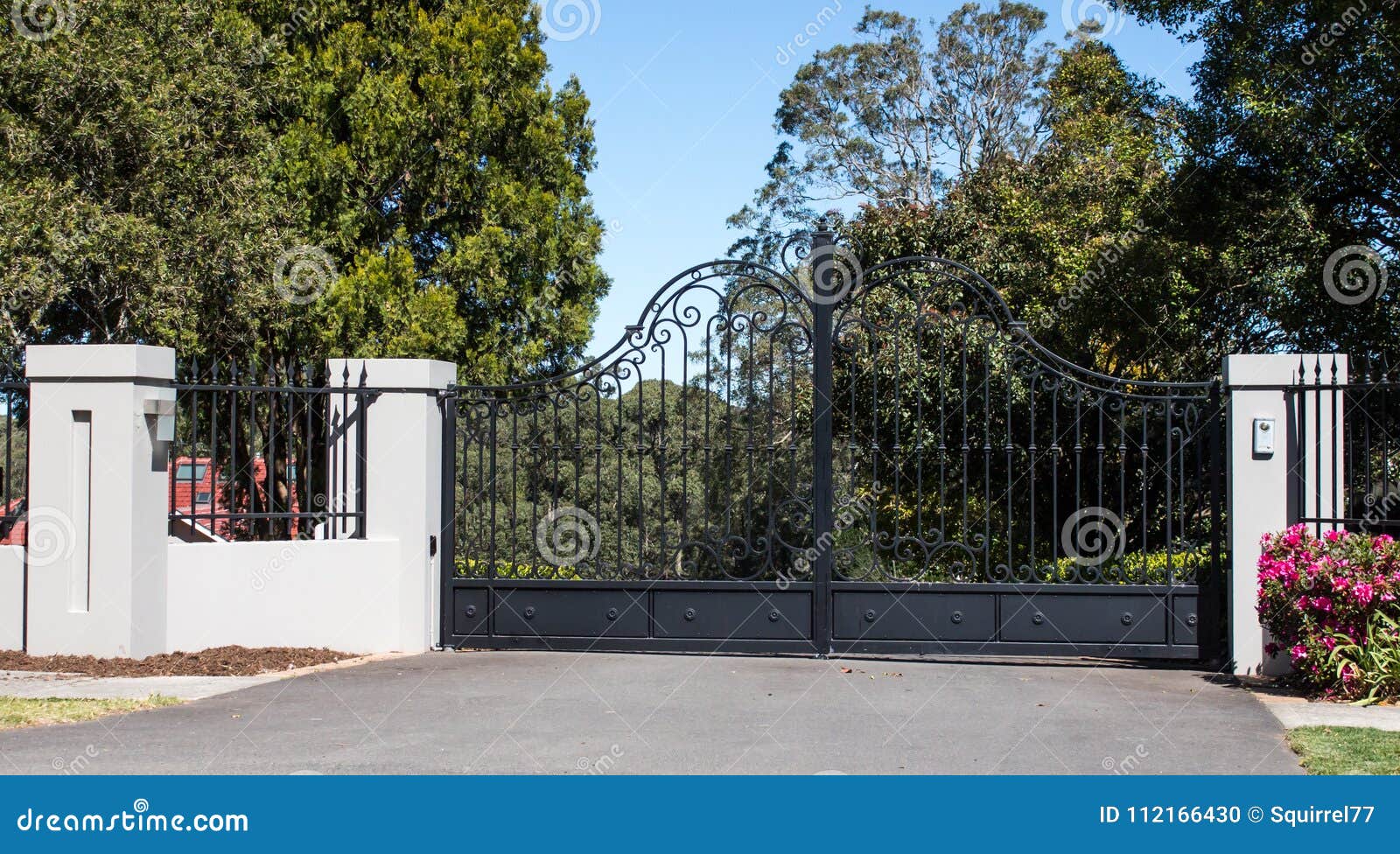 metal driveway entrance gates set in brick fence with garden trees in background