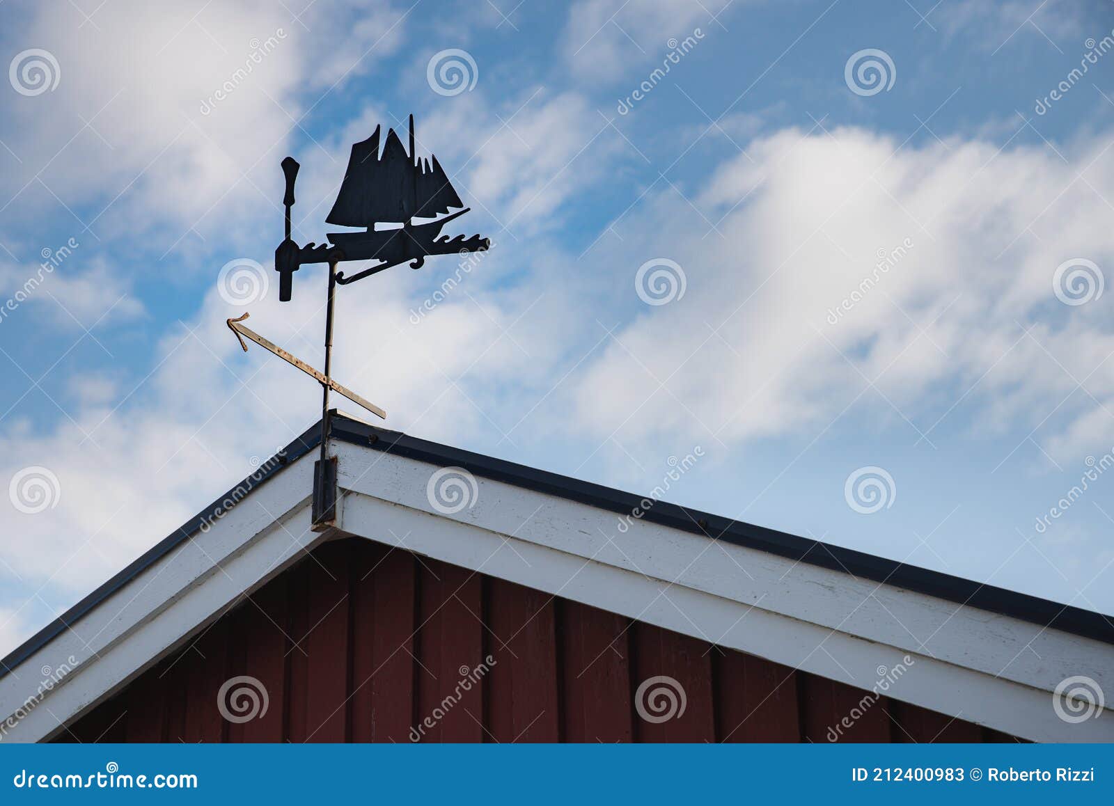 a metallic weather vane on a scandinavian summerhouse pitched roof resembles an ancient viking sailing ship or three mast galley