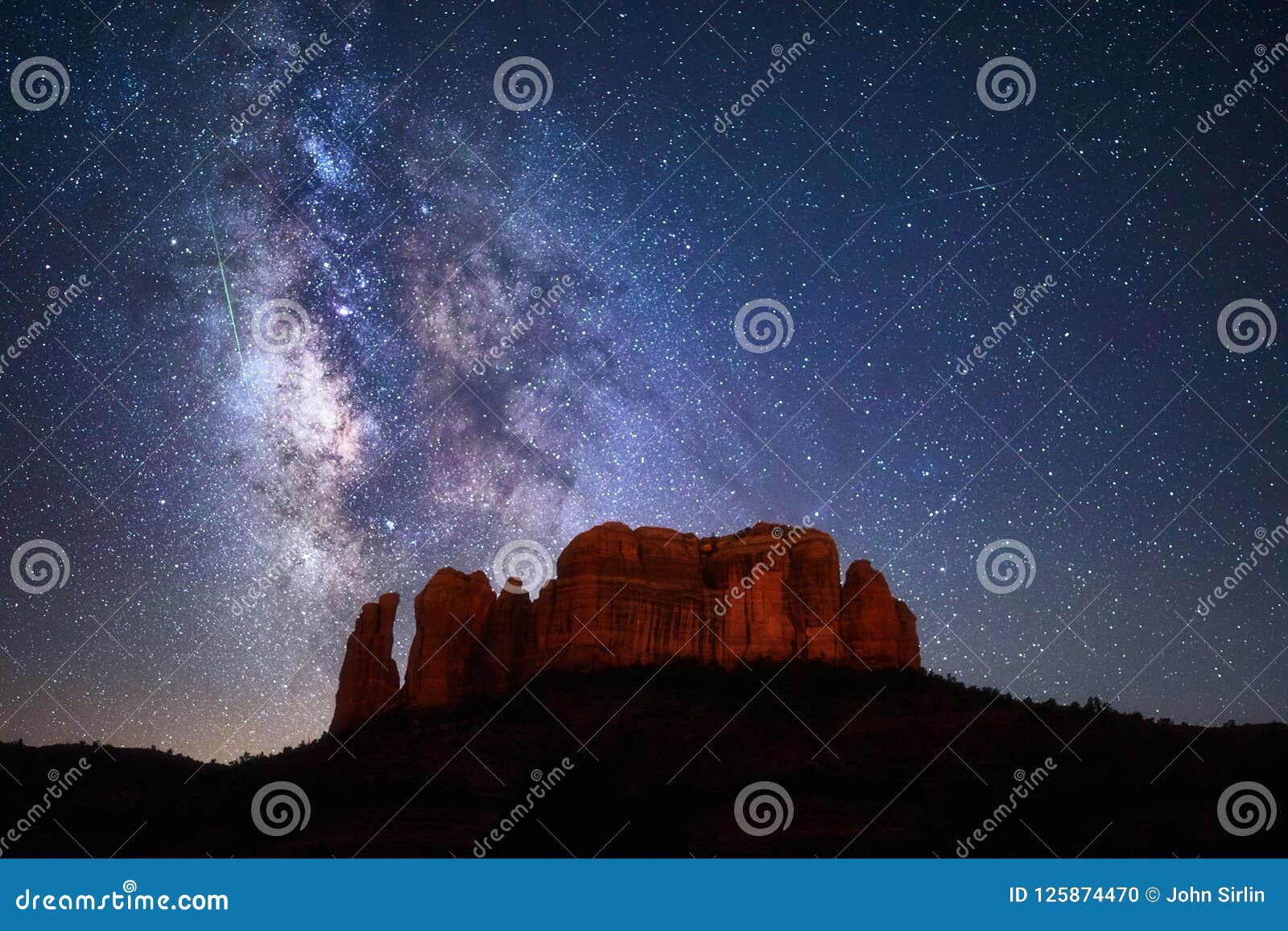 a meteor streaks through the milky way above cathedral rock in sedona, arizona.