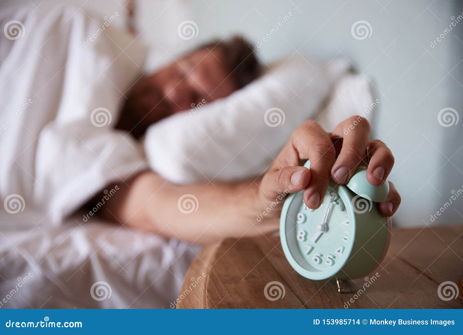 Mid Adult Man Asleep In Bed Reaching Out To Alarm Clock On The Bedside