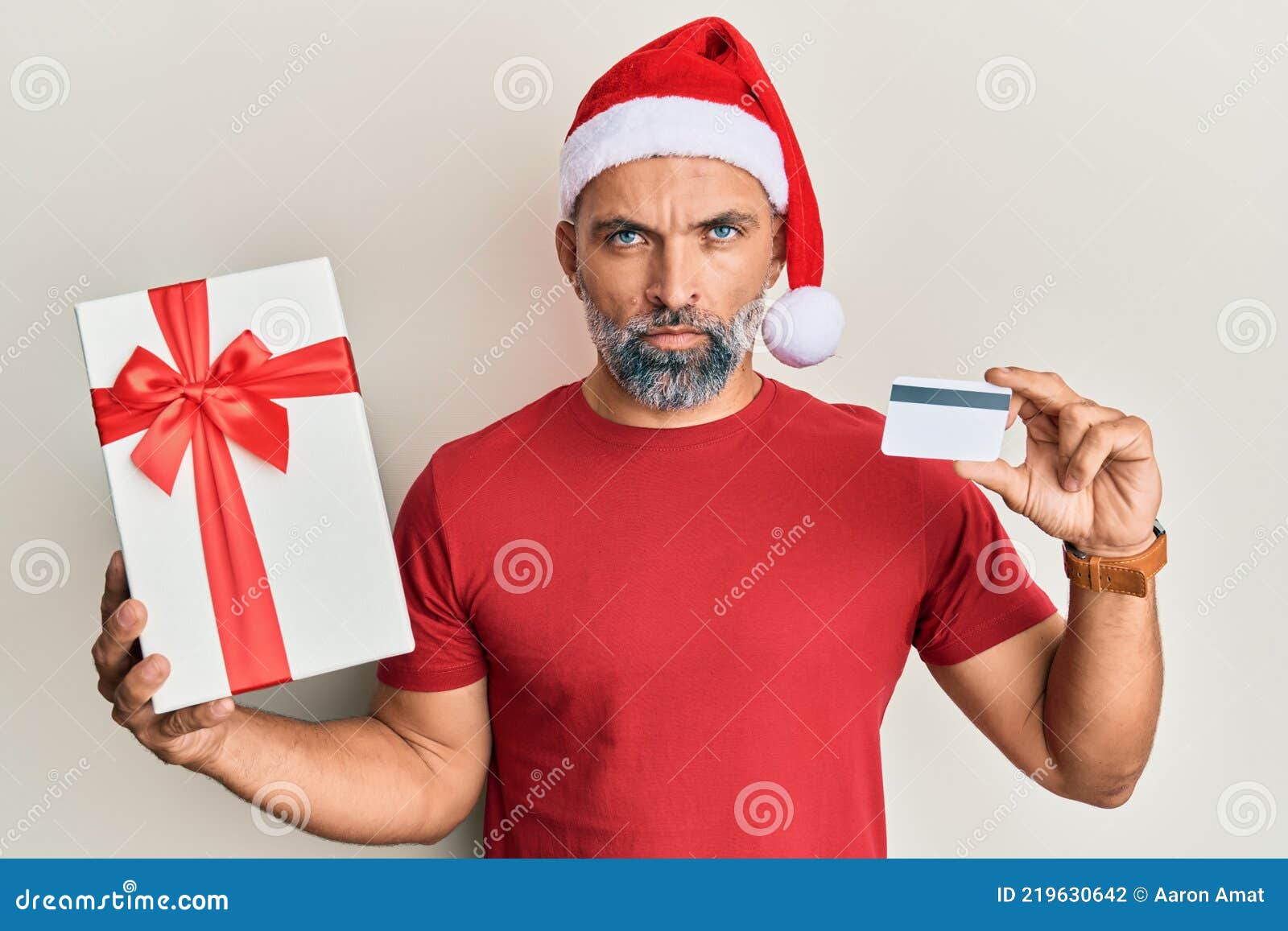 middle age handsome man wearing chrismast hat holding gift and credit card skeptic and nervous, frowning upset because of problem