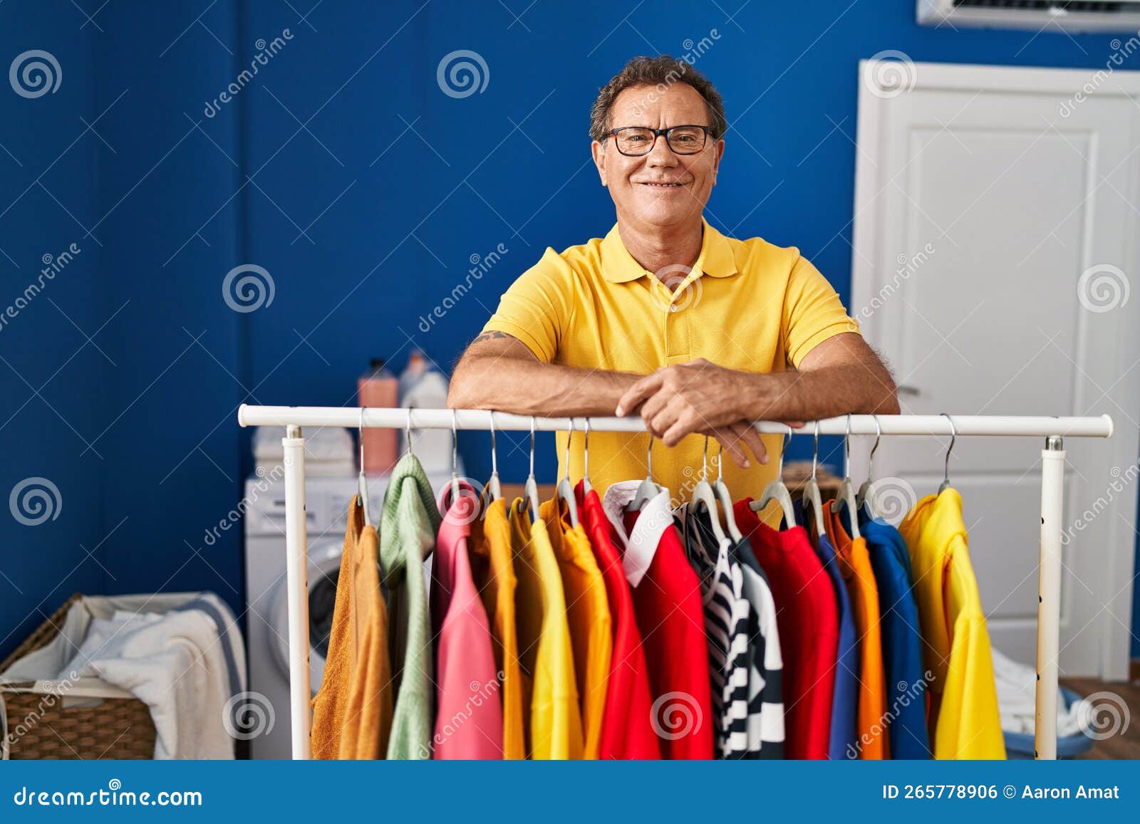 Middle Age Man Smiling Confident Leaning on Clothes Rack at Laundry