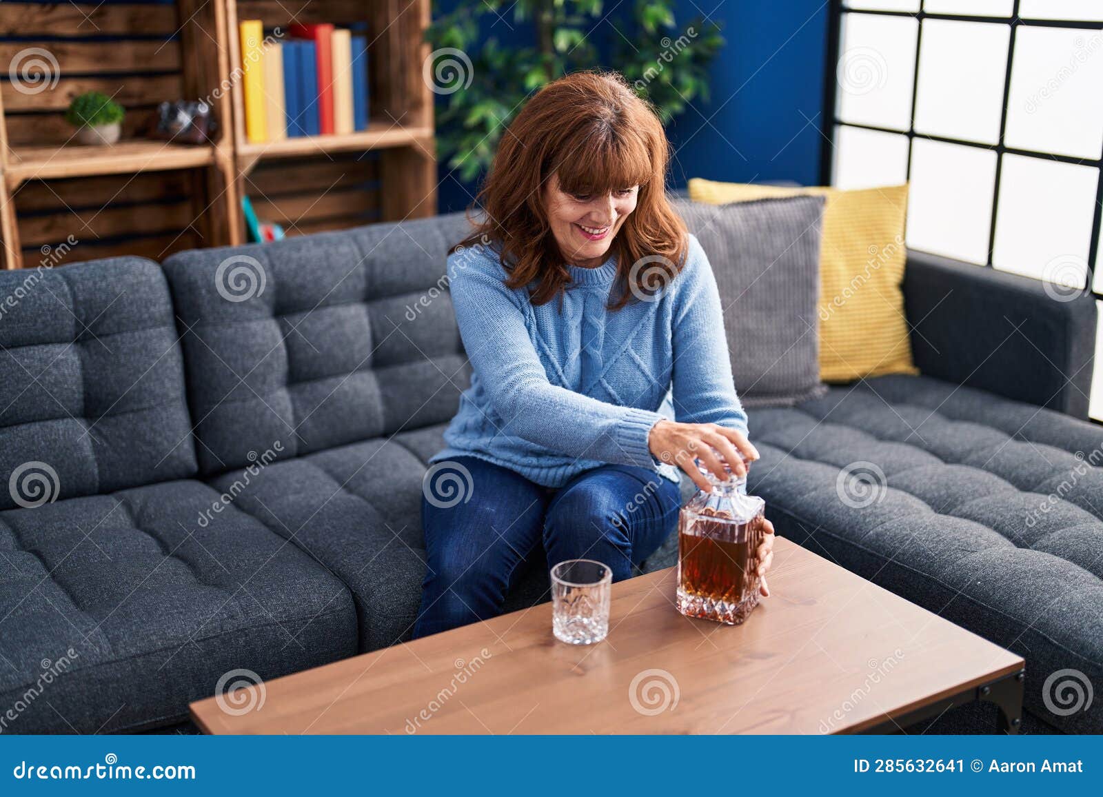 middle age woman drinking licor sitting on sofa at home
