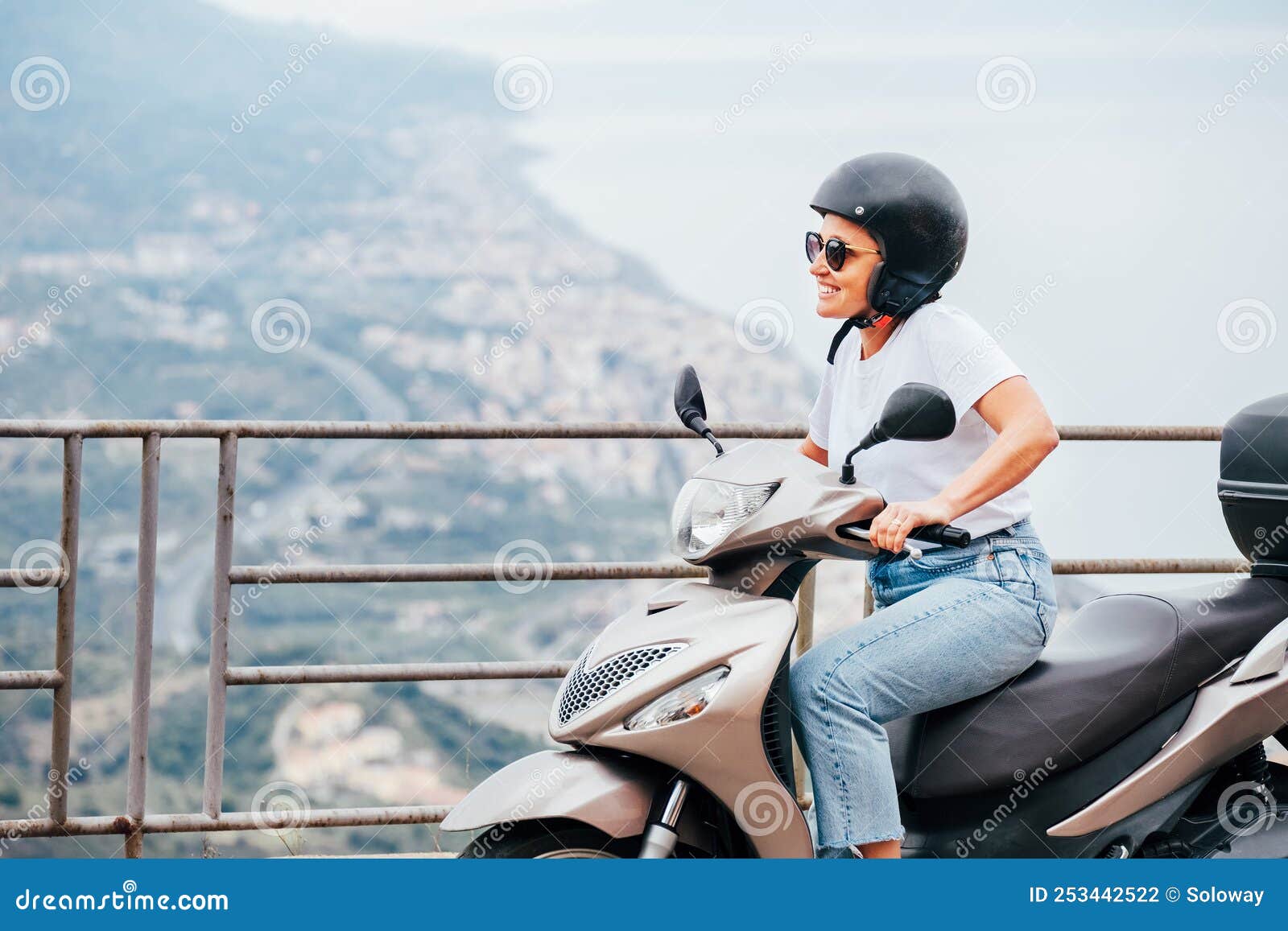 middle-age woman in helmet and sunglasses on motor scooter on the sicilian old town streets in the forza d`agro with sant`alessi