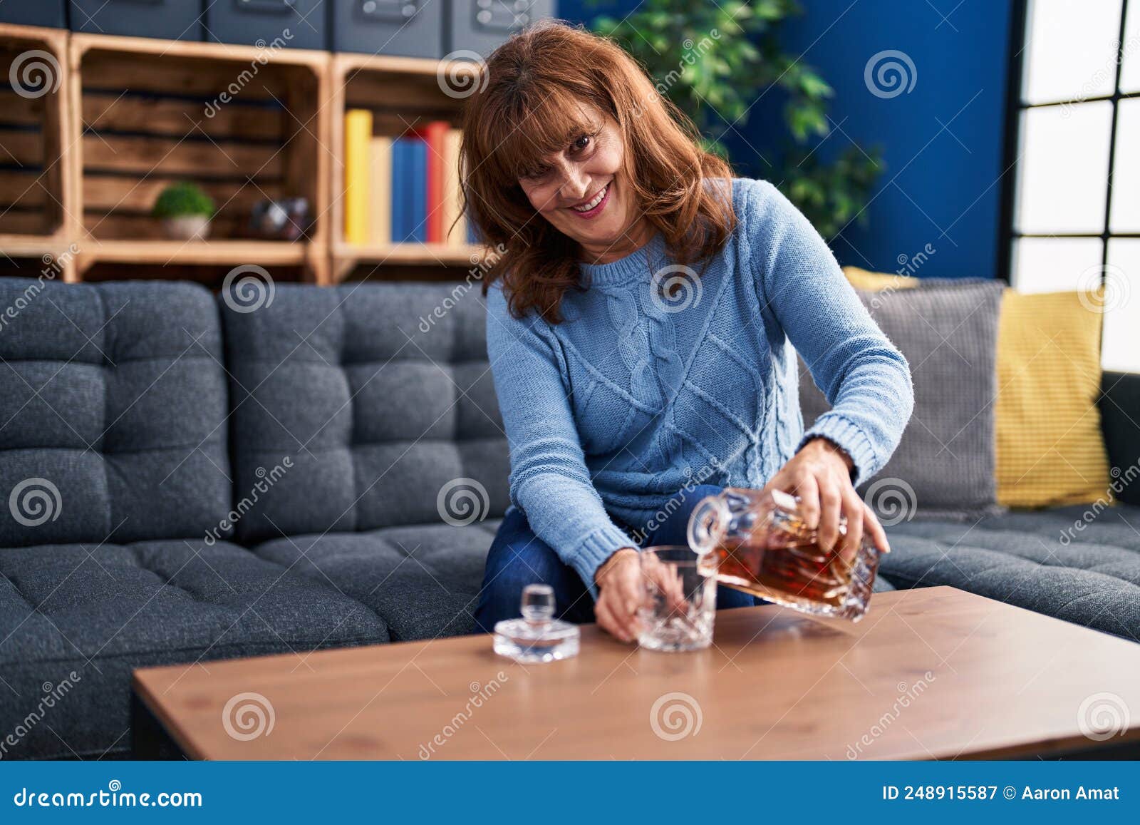middle age woman pouring licor on glass sitting on sofa at home