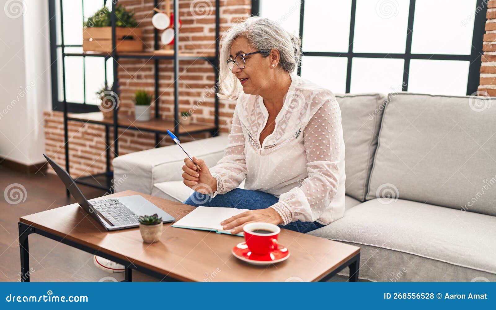 Middle Age Woman Studying Using Laptop Writing on Book at Home Stock
