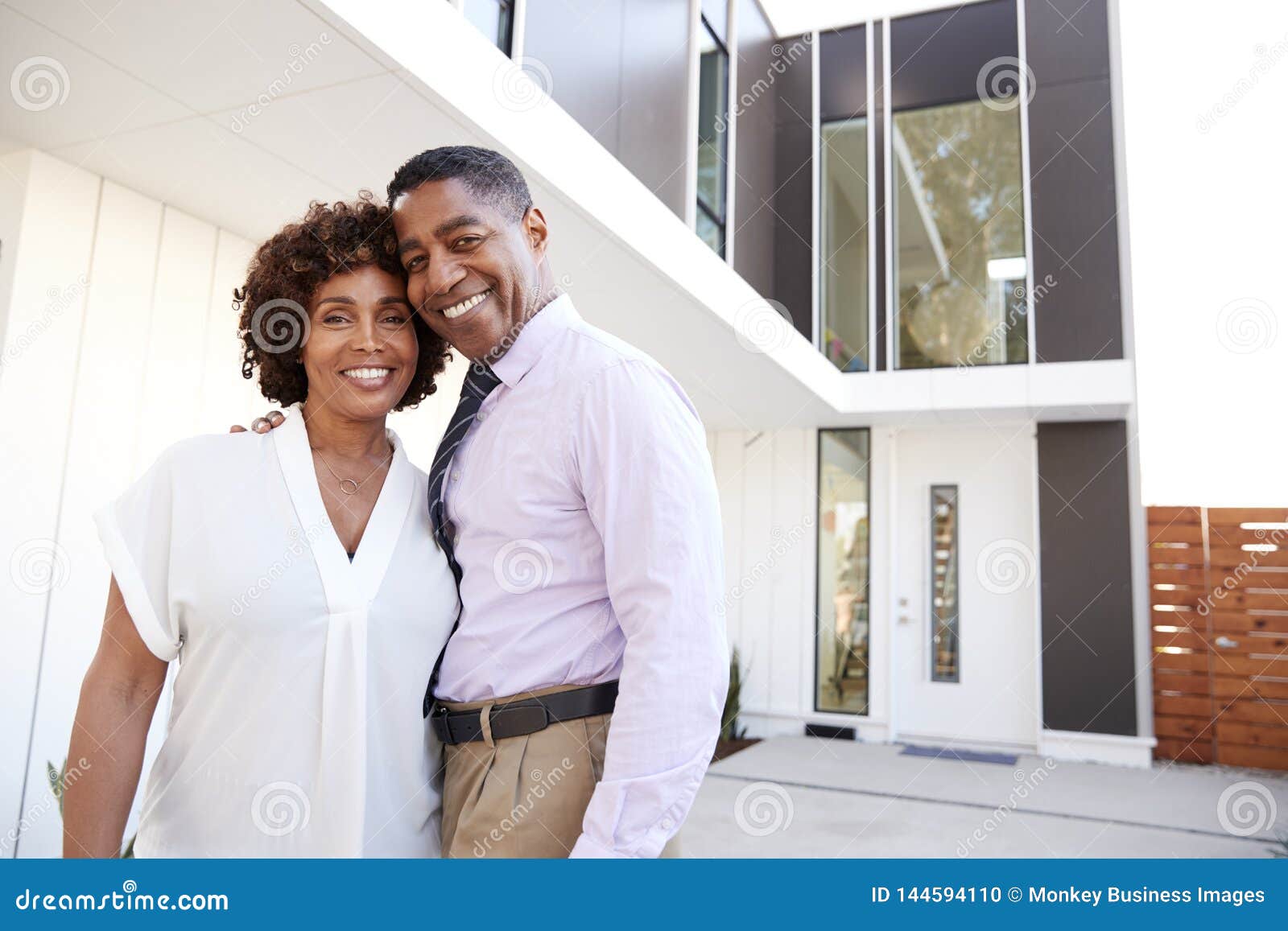 middle aged african american  couple stand outside admiring their modern home, back view