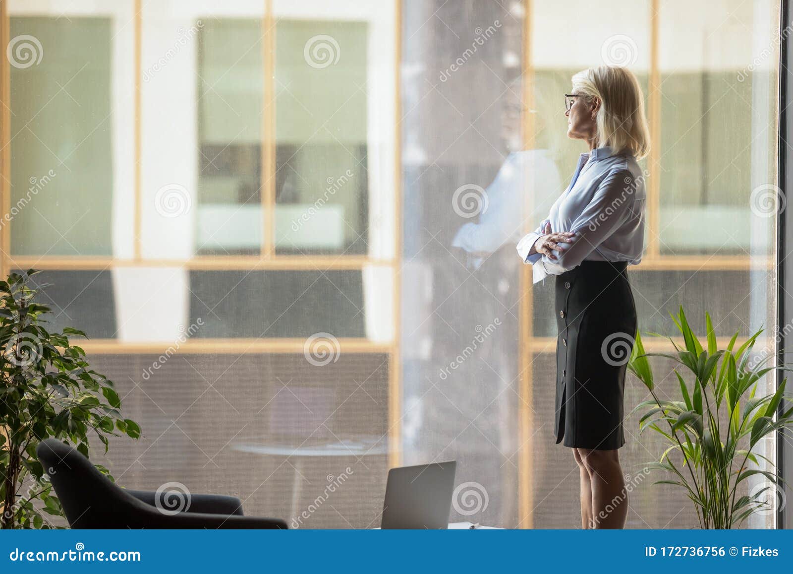 aged businesswoman looking out window dreaming about corporate goals realizations