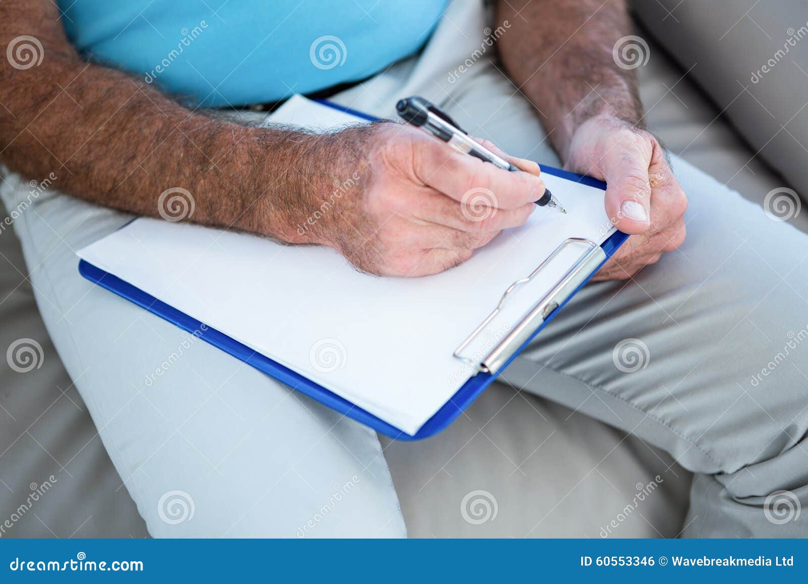 Midsection of senior man writing on clipboard at home.
