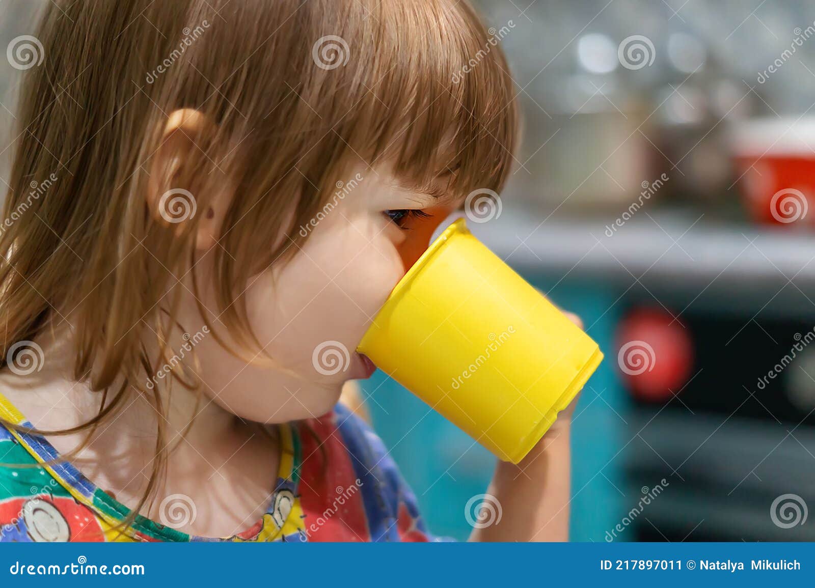 Mignonne Petite Fille Buvant Du Lait Chaud D'une Tasse Jaune Vue De Côté.  Un Bébé Affamé Prend Son Petit Déjeuner à La Table à Man Image stock -  Image du sain, main