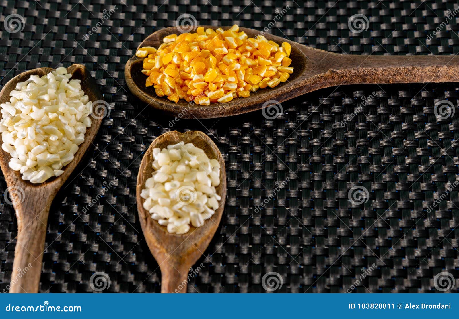 milho de cor branca e amarela para preparar canjica servida em colheres de madeira sobre um fundo escuro
