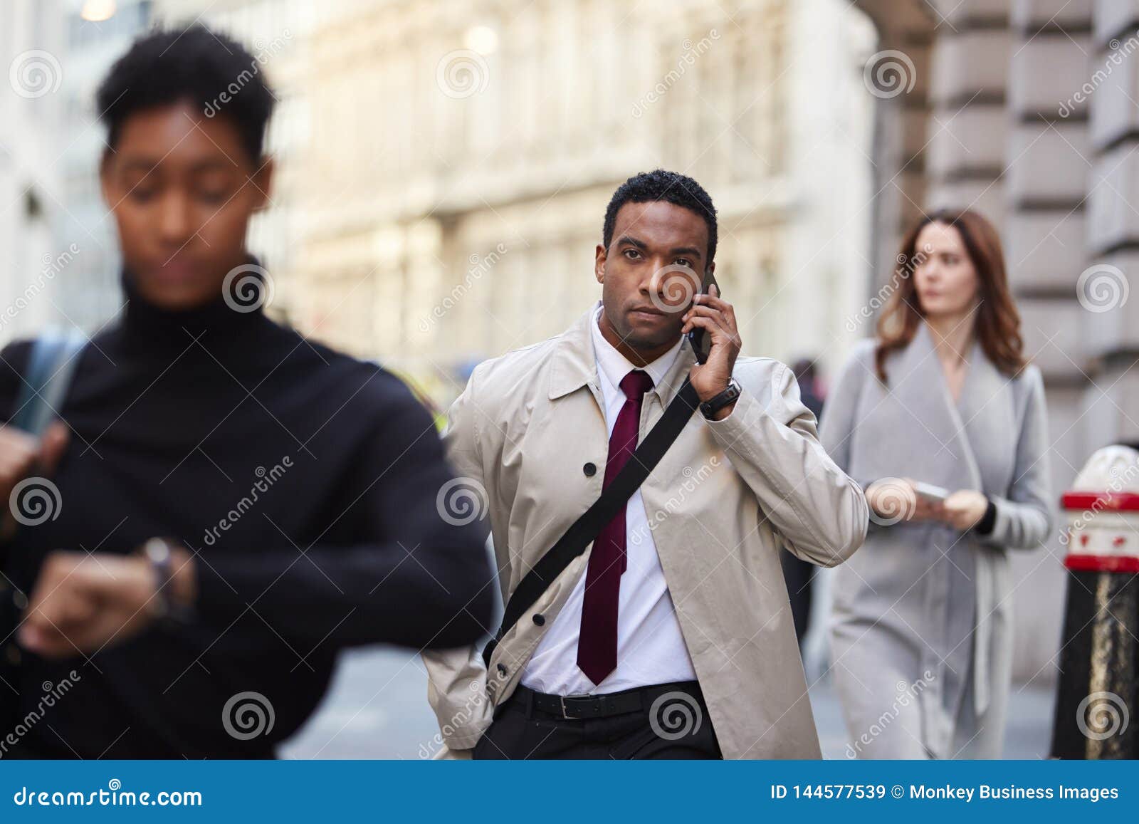 millennial black businessman walking in a busy london street using smartphone, selective focus