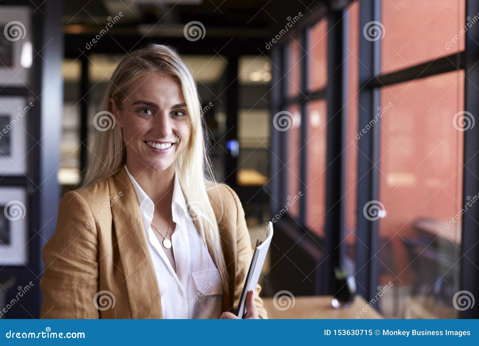 millennial white blonde businesswoman smiling to camera by the window in an office, close up
