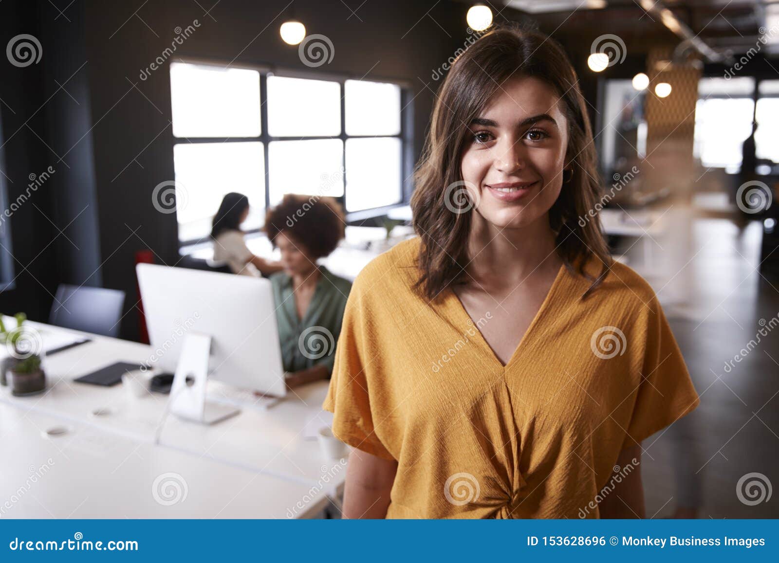 millennial white female creative standing in a busy casual office, smiling to camera