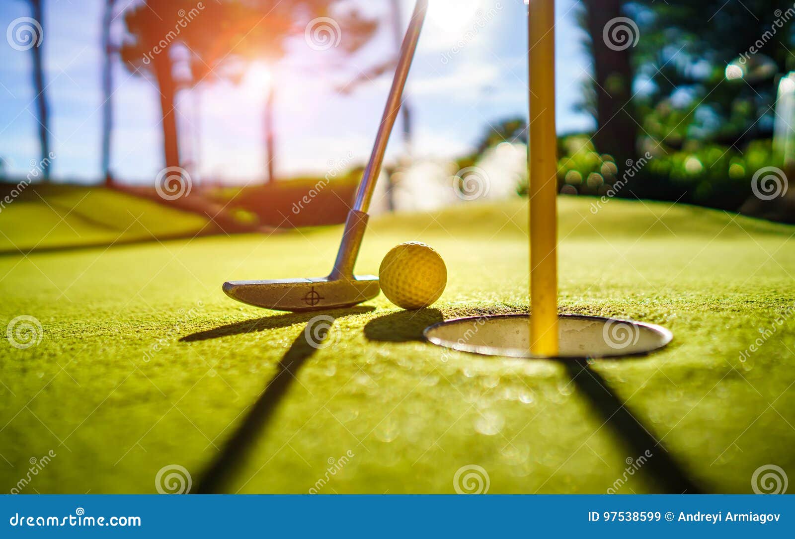 mini golf yellow ball with a bat near the hole at sunset