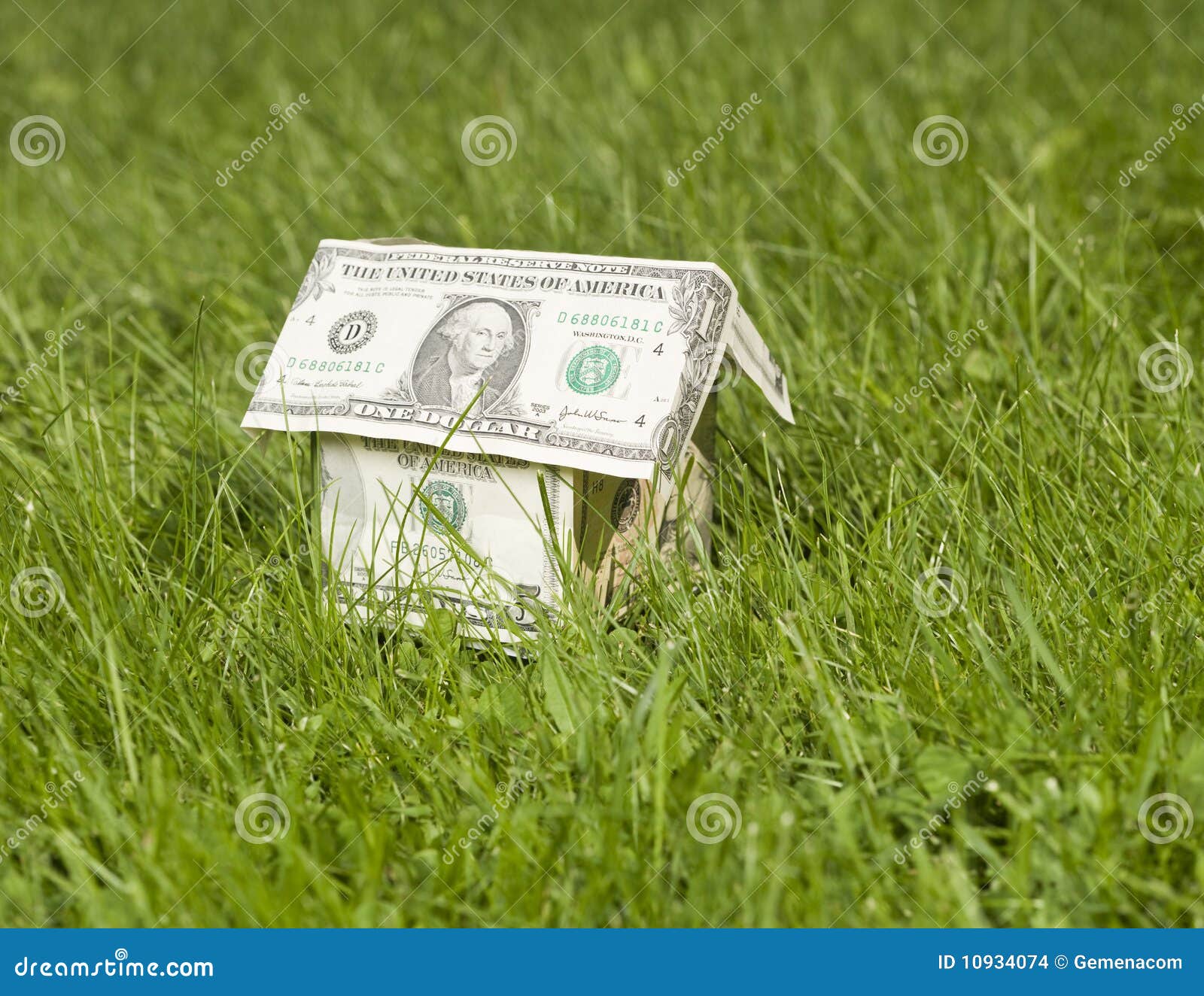 A miniature house made of dollar bills outside in the grass.