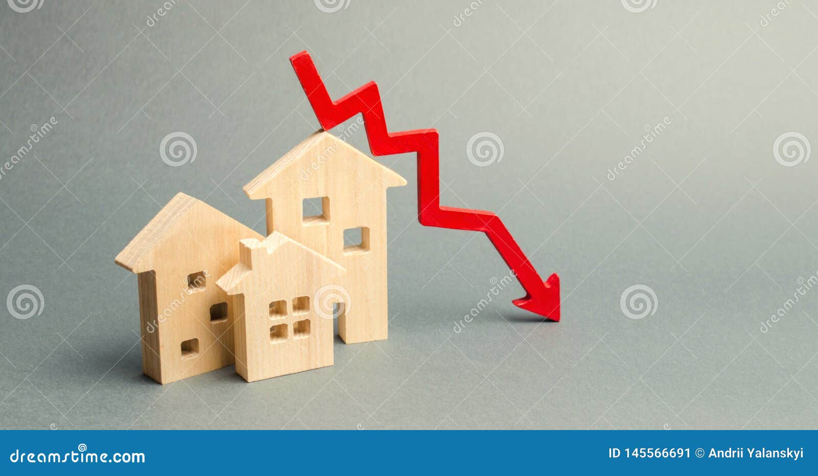 miniature wooden houses and a red arrow down. the concept of low cost real estate. lower mortgage interest rates. falling prices
