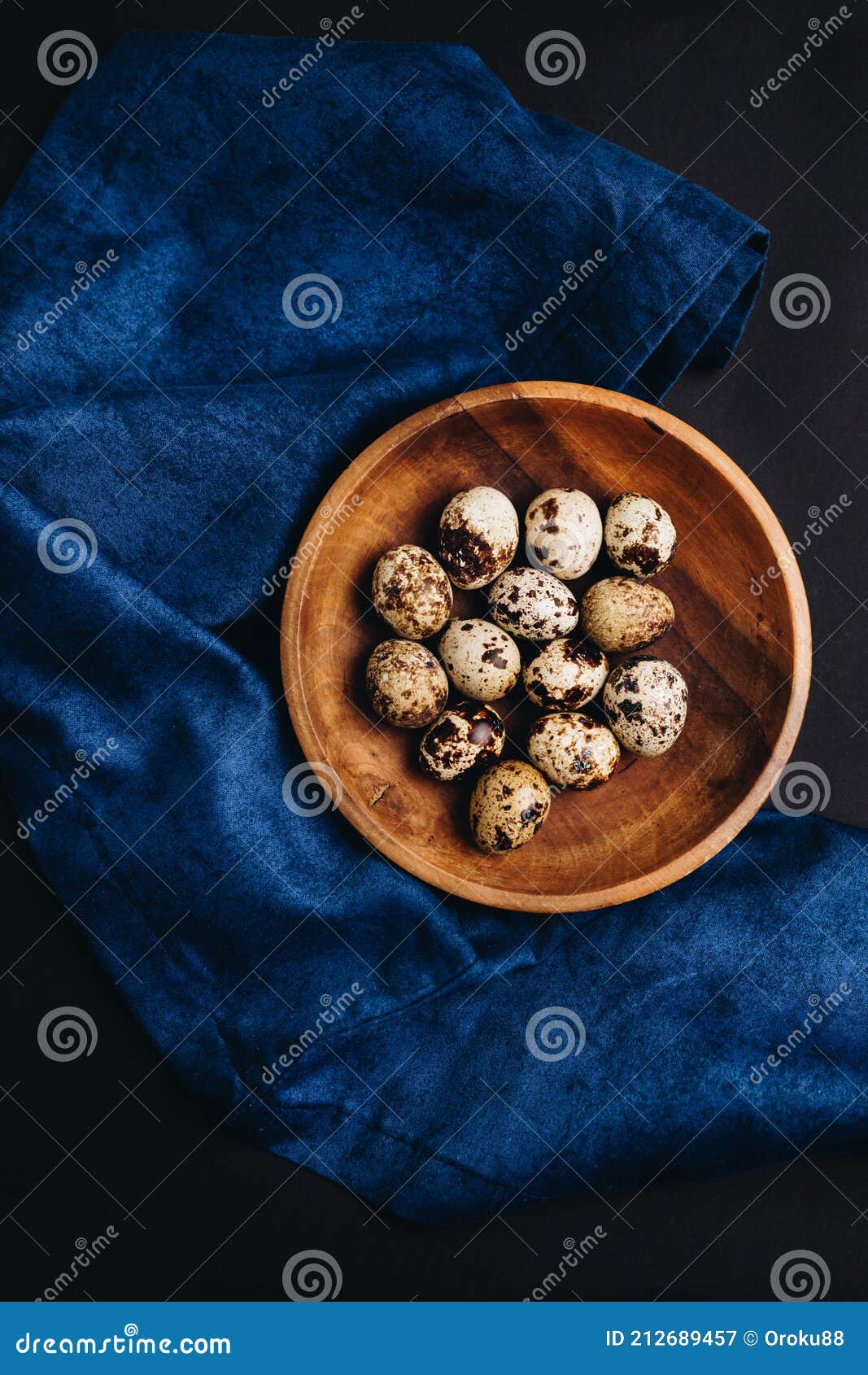 minimal art of fresh quail eggs in the wooden bowl on the dark background with blue saten or silk around