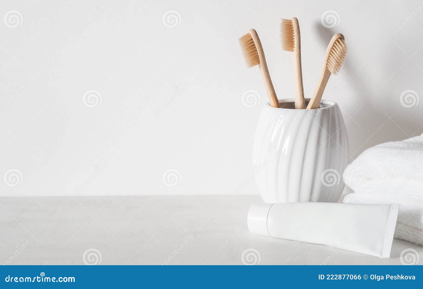 minimal bath background with bamboo toothbrushs in ceramic glass, white tube of toothpaste and white towels