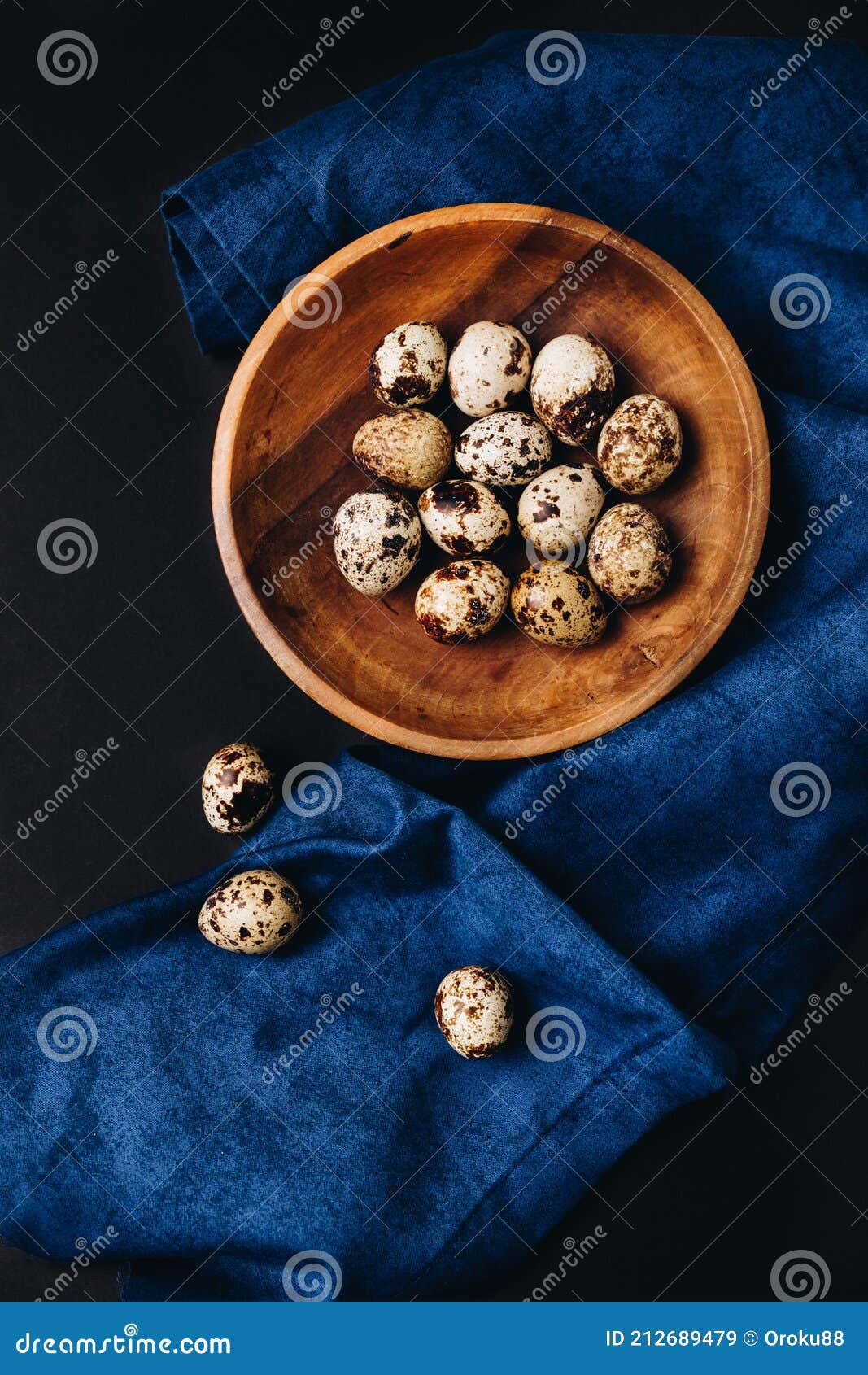minimal concept of fresh quail eggs in the wooden bowl on the dark background with blue saten or silk around